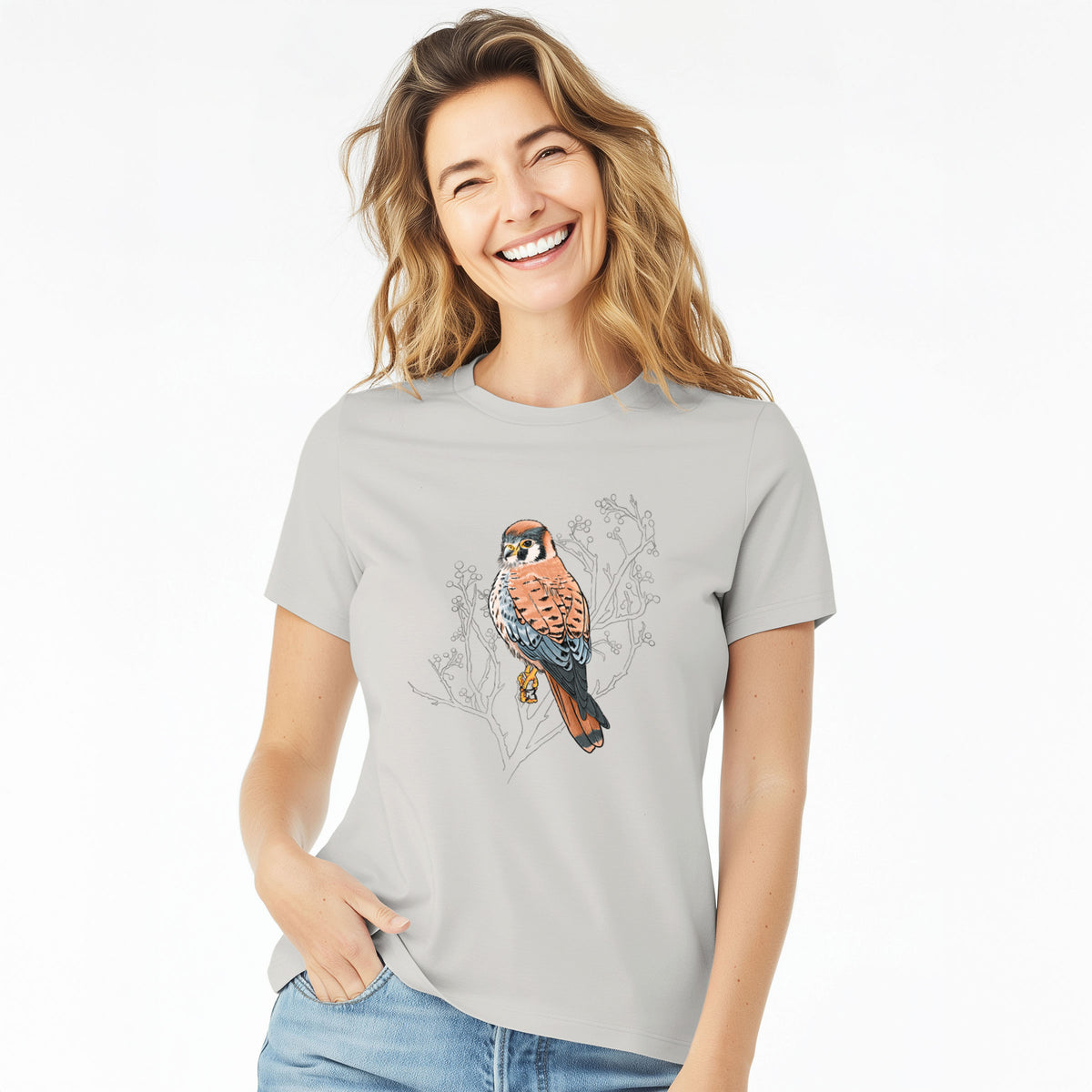 Woman wearing a lunar grey women's relaxed fit cotton t-shirt printed with a full-color illustration of an American kestrel perched among pale branches.