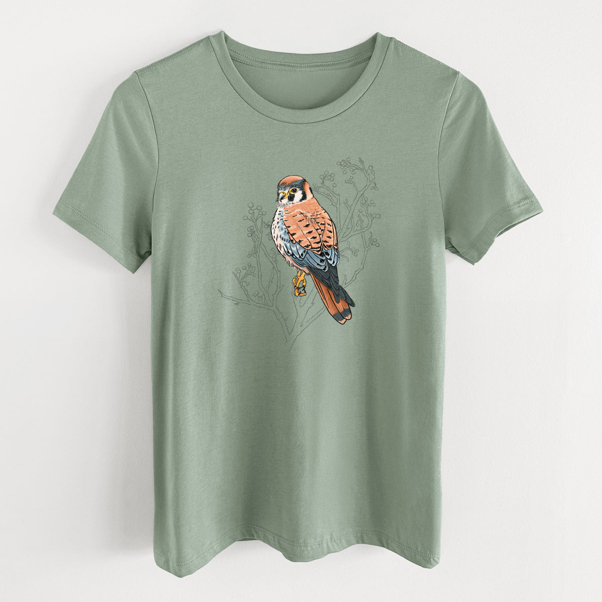 Sage green women's relaxed fit cotton t-shirt laid flat, printed with a full-color illustration of an American kestrel perched among pale branches.