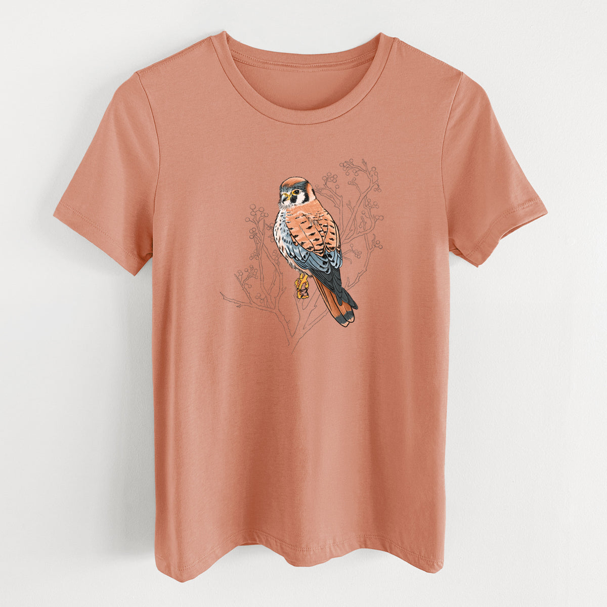 Terracotta orange women's relaxed fit cotton t-shirt laid flat, printed with a full-color illustration of an American kestrel perched among pale branches.