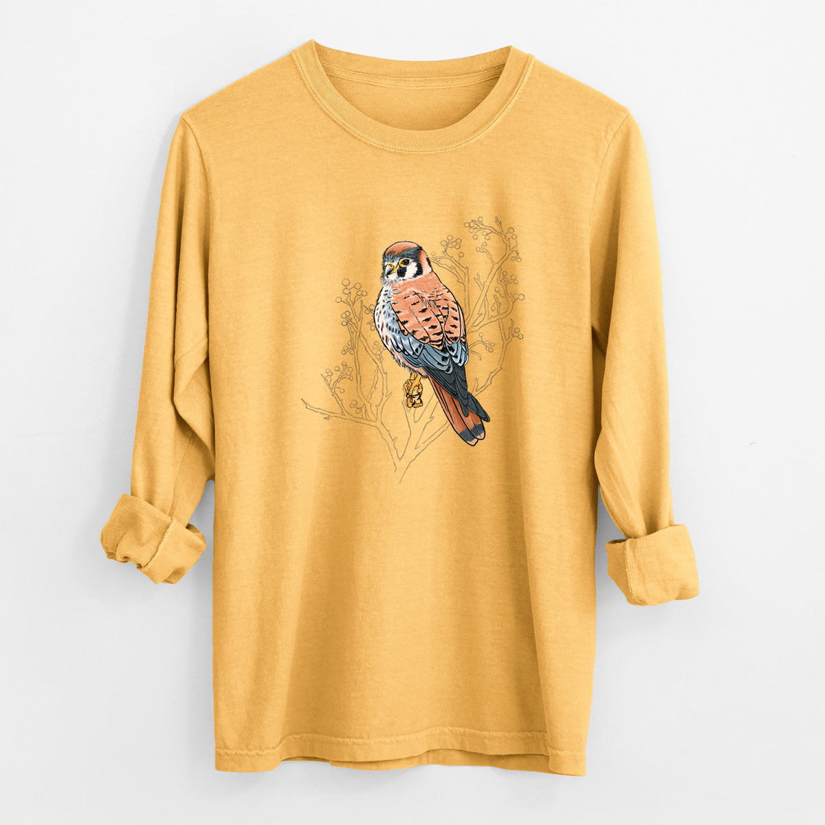 Golden wheat yellow Comfort Colors long sleeve shirt laid flat with the cuffs rolled, printed with a full-color illustration of an American kestrel perched among pale branches.