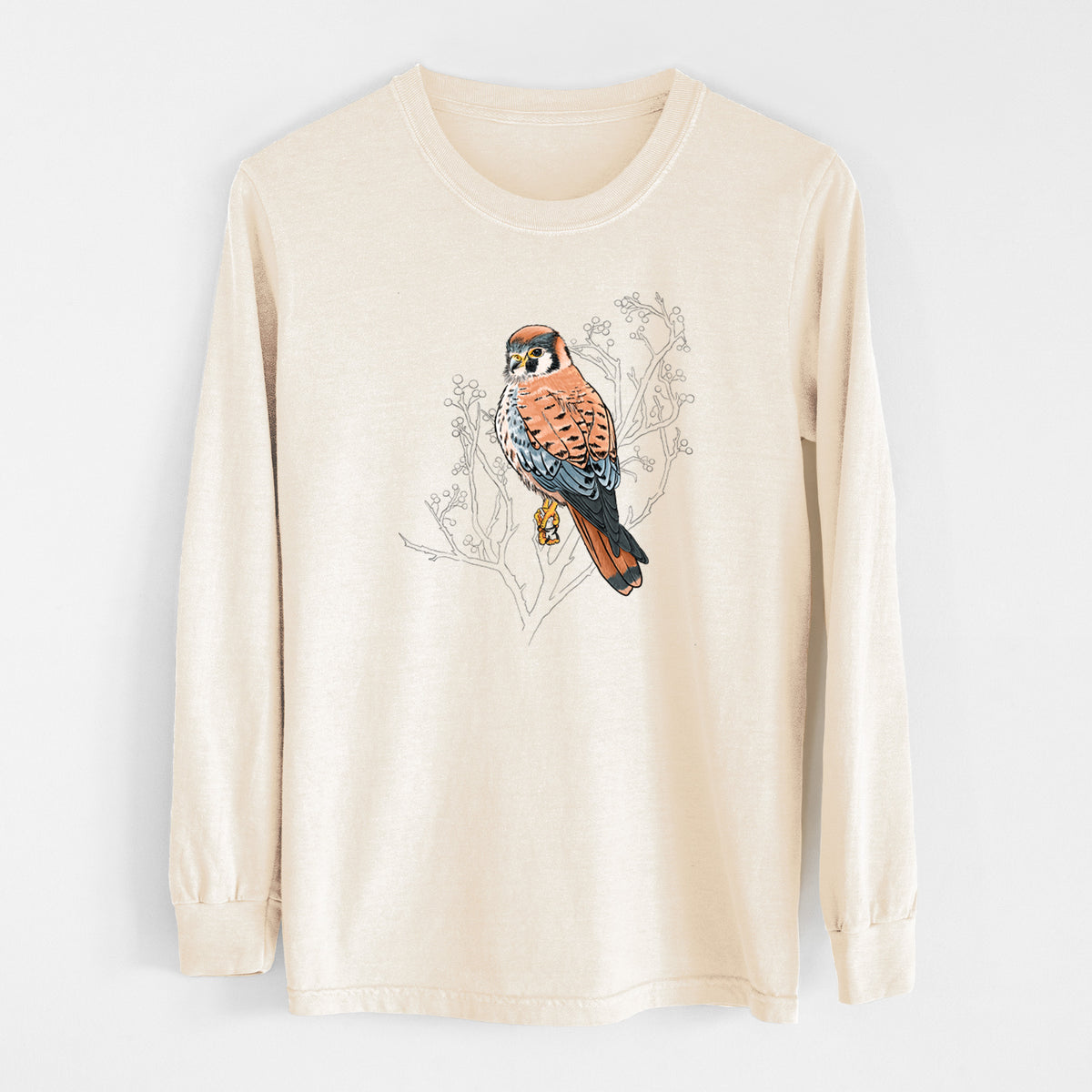 Ivory Comfort Colors long sleeve shirt laid flat, printed with a full-color illustration of an American kestrel perched among pale branches.