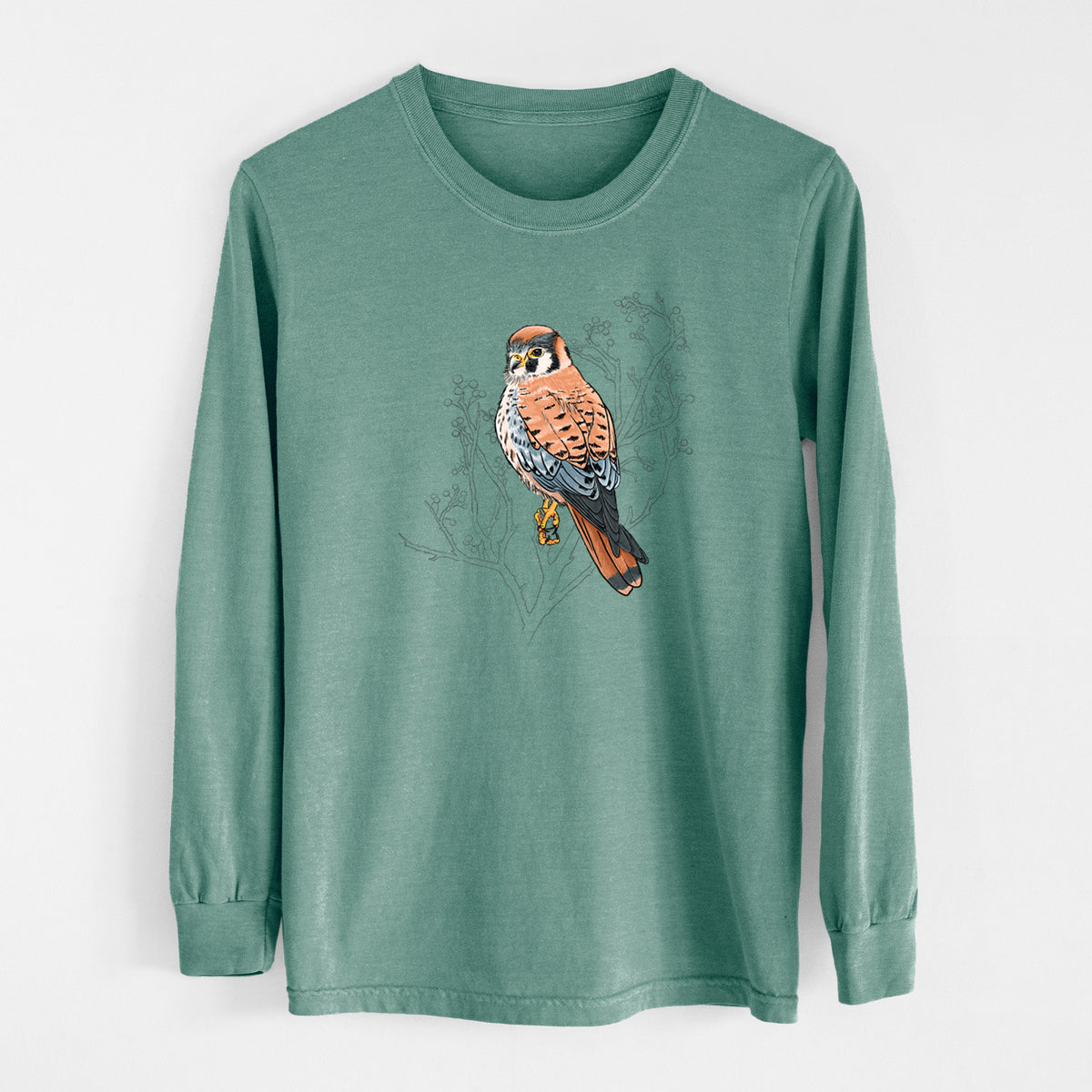 Pine green Comfort Colors long sleeve shirt laid flat, printed with a full-color illustration of an American kestrel perched among pale branches.