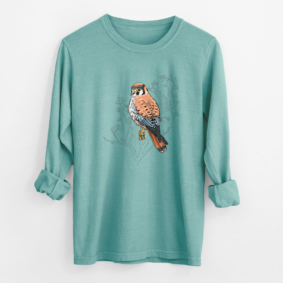 Reef green Comfort Colors long sleeve shirt laid flat with the cuffs rolled, printed with a full-color illustration of an American kestrel perched among pale branches.