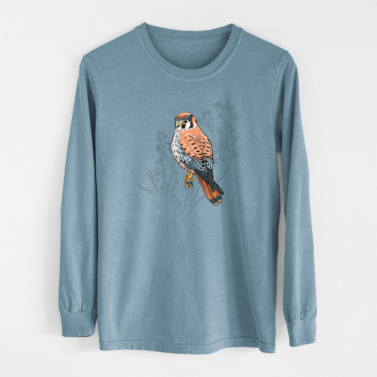 Steel blue Comfort Colors long sleeve shirt laid flat, printed with a full-color illustration of an American kestrel perched among pale branches.