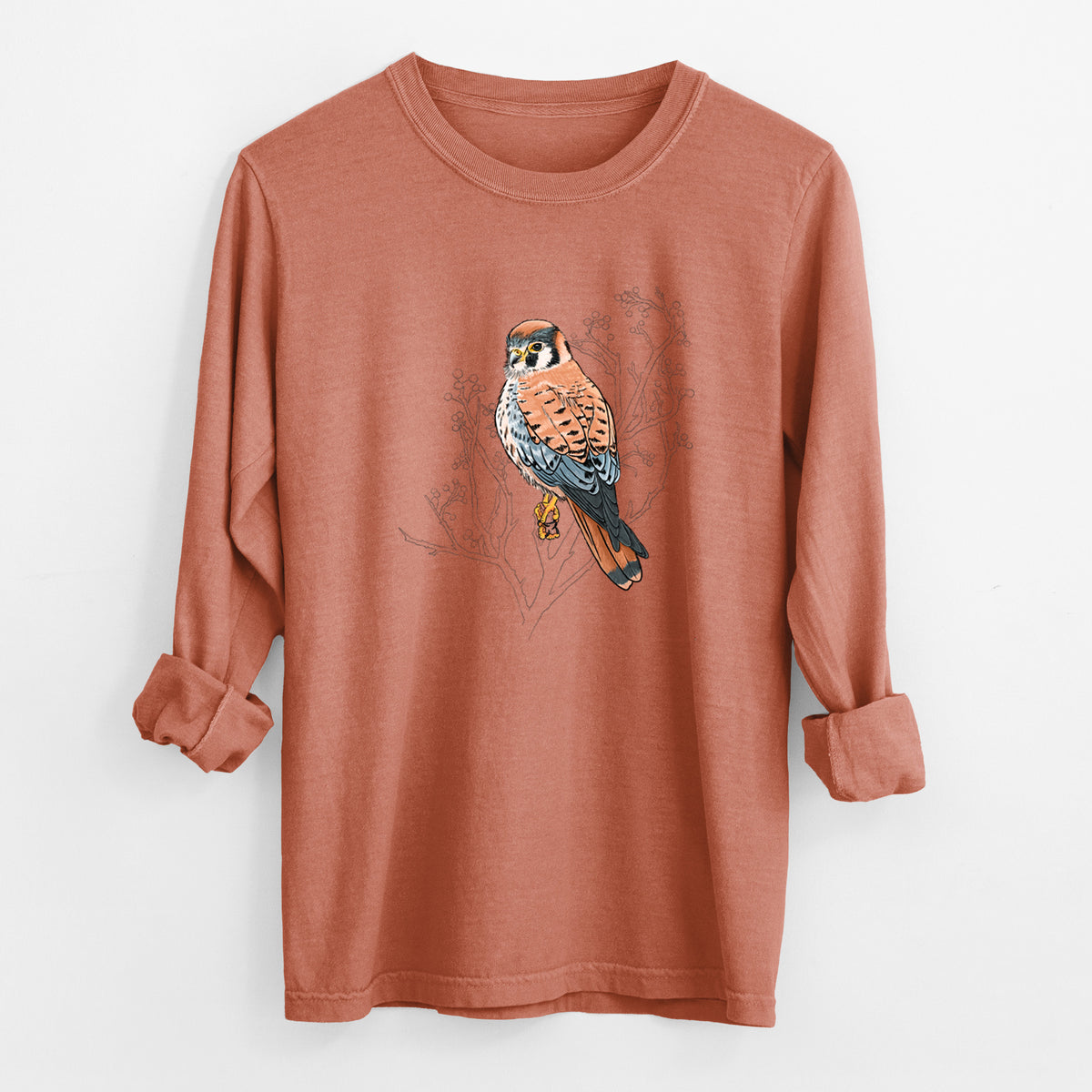 Yam burnt orange Comfort Colors long sleeve shirt laid flat with the cuffs rolled, printed with a full-color illustration of an American kestrel perched among pale branches.