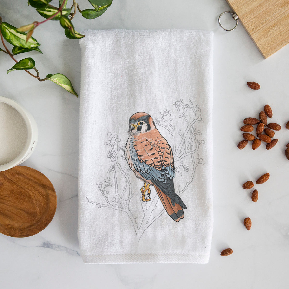 White hand towel printed with a full-color illustration of an American kestrel perched among pale branches.