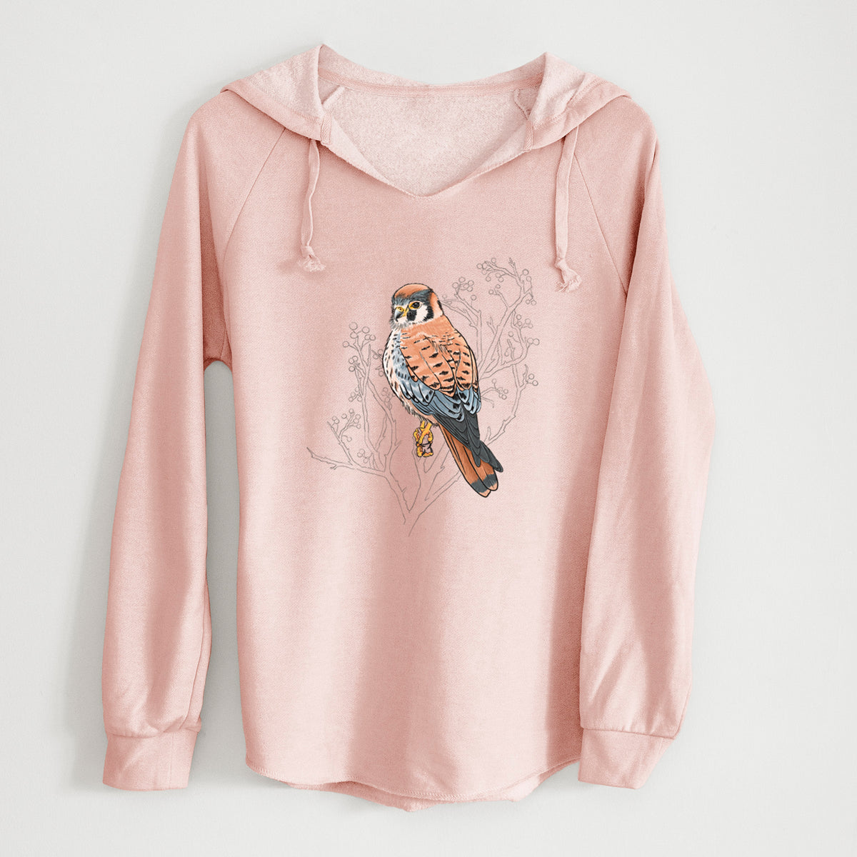 Blush pink women's Cali Wave hooded sweatshirt laid flat, printed with a full-color illustration of an American kestrel perched among pale branches.