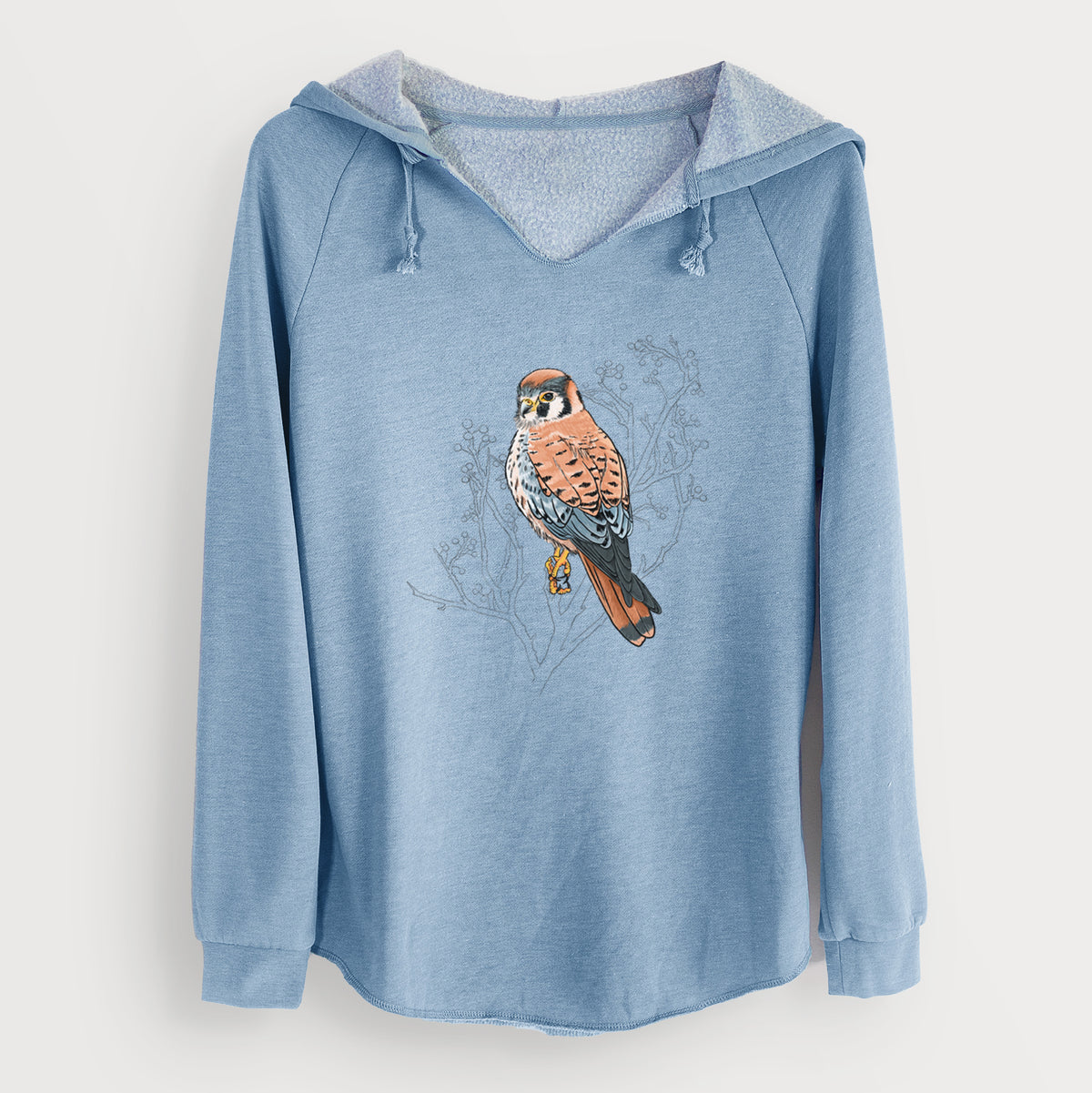 Misty blue women's Cali Wave hooded sweatshirt laid flat, printed with a full-color illustration of an American kestrel perched among pale branches.