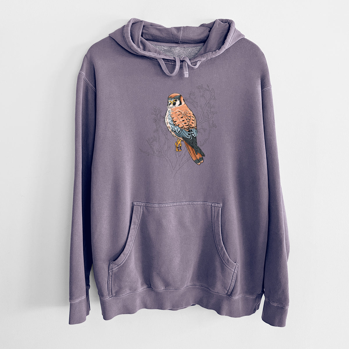 Plum purple pigment dyed hoodie laid flat, printed with a full-color illustration of an American kestrel perched among pale branches.