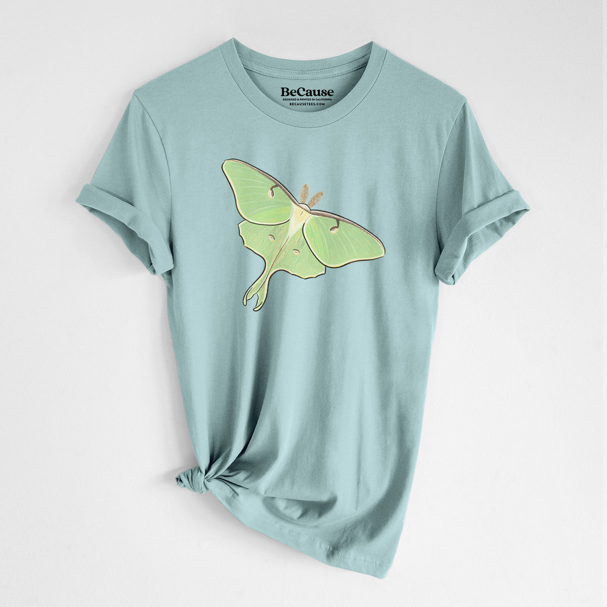 Dusty blue lightweight cotton t-shirt laid flat with the sleeves rolled, printed with a full-color illustration of a pale green luna moth with long tails on its wings.