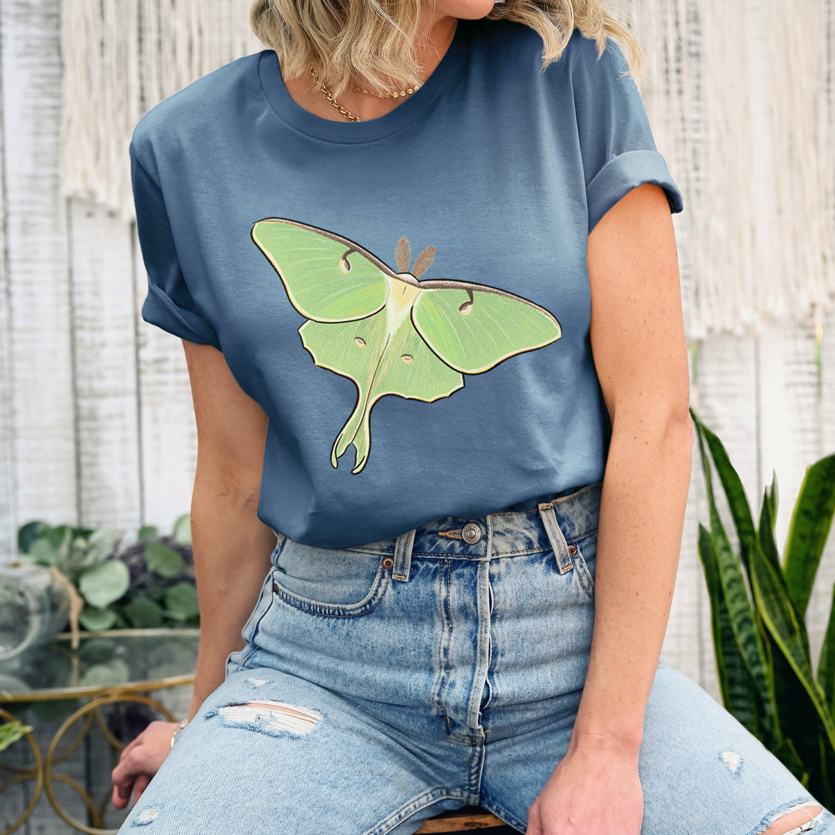 Woman wearing a steel blue lightweight cotton t-shirt printed with a full-color illustration of a pale green luna moth with long tails on its wings.