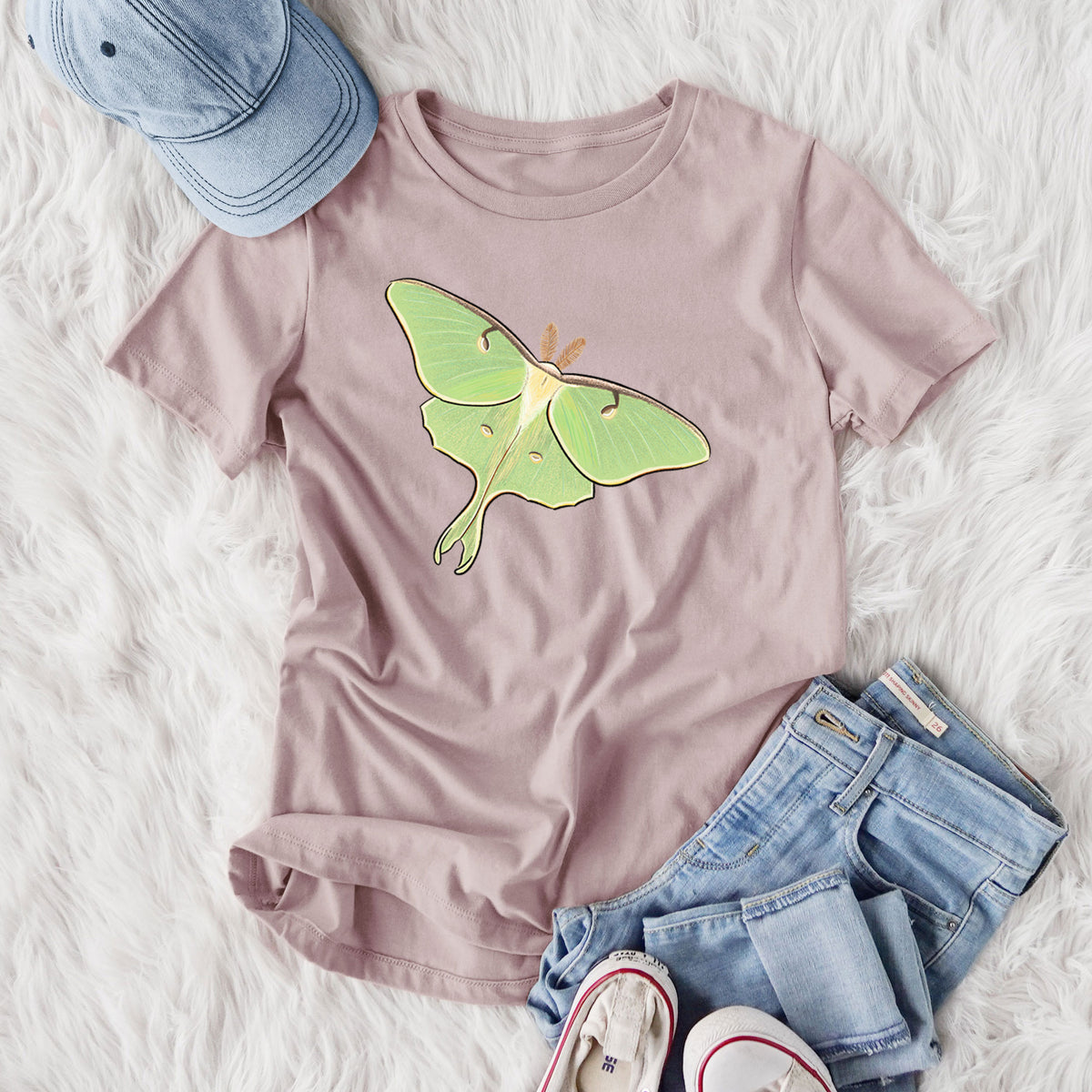 Women's relaxed fit cotton t-shirt printed with a full-color illustration of a pale green luna moth with long tails on its wings, styled flat on a white faux fur rug with jeans.