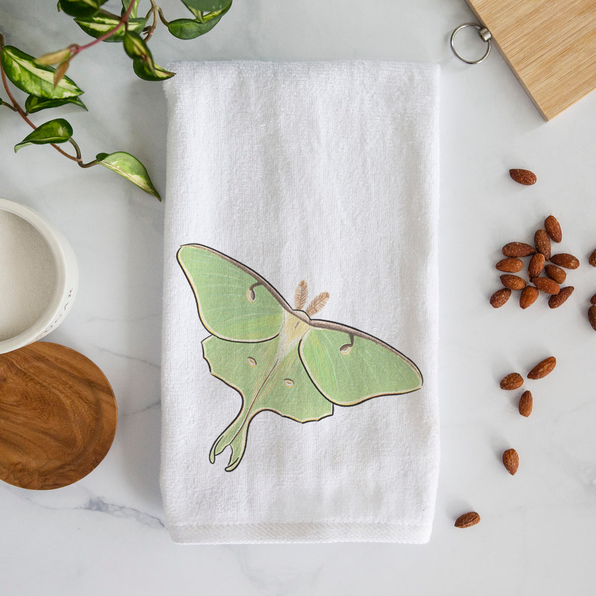 White hand towel printed with a full-color illustration of a pale green luna moth with long tails on its wings.