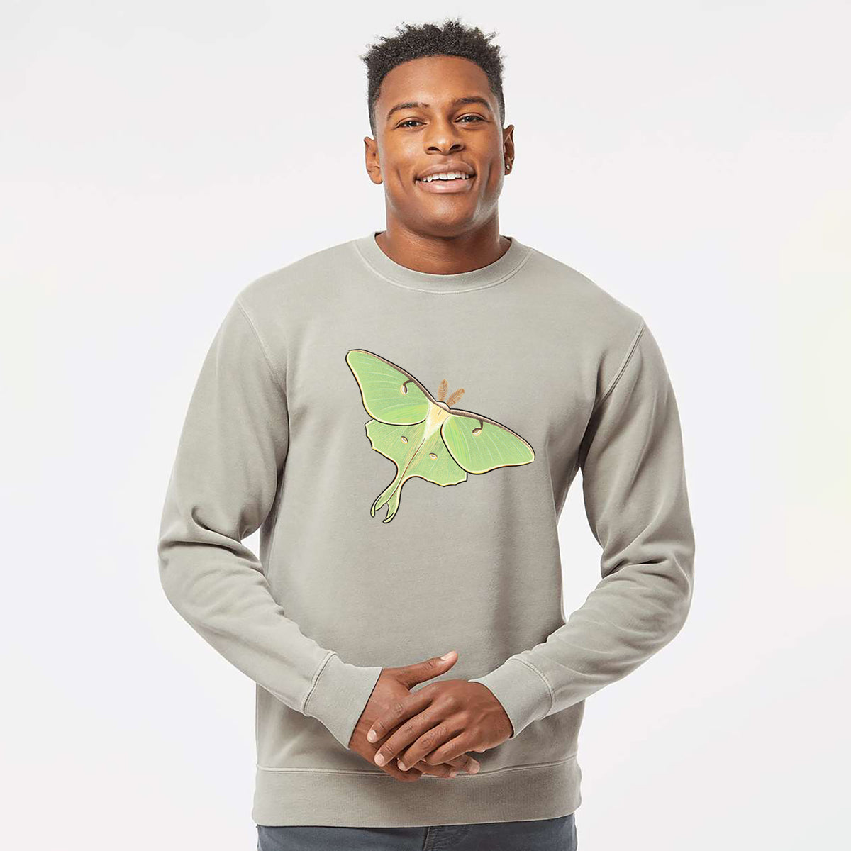 Model wearing a cement grey pigment dyed crewneck sweatshirt printed with a full-color illustration of a pale green luna moth with long tails on its wings.