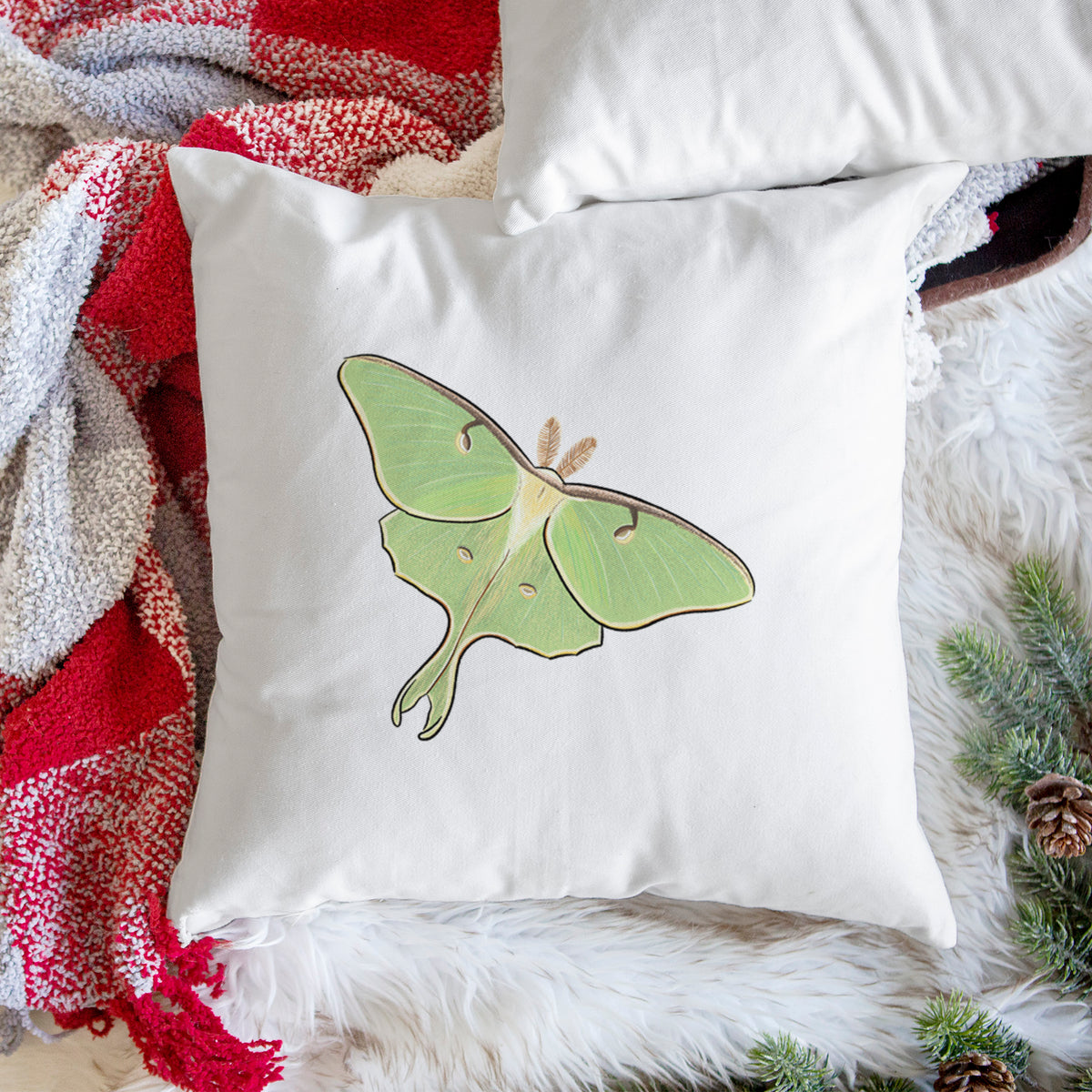 White pillow cover printed with a full-color illustration of a pale green luna moth with long tails on its wings, on a woven chair.