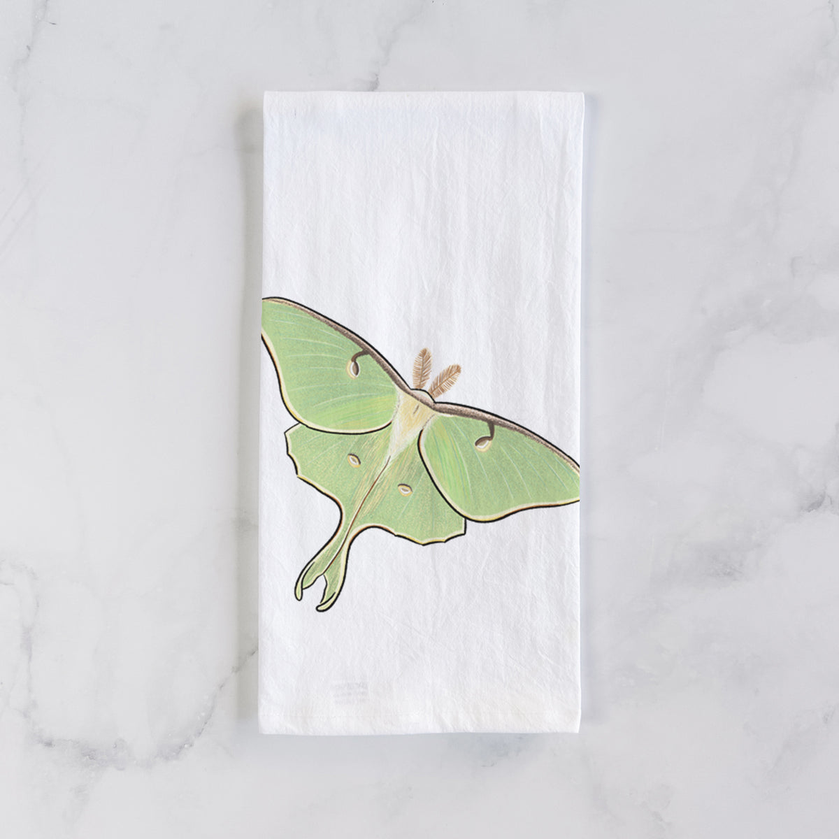 White cotton tea towel laid flat on marble, printed with a full-color illustration of a pale green luna moth with long tails on its wings.