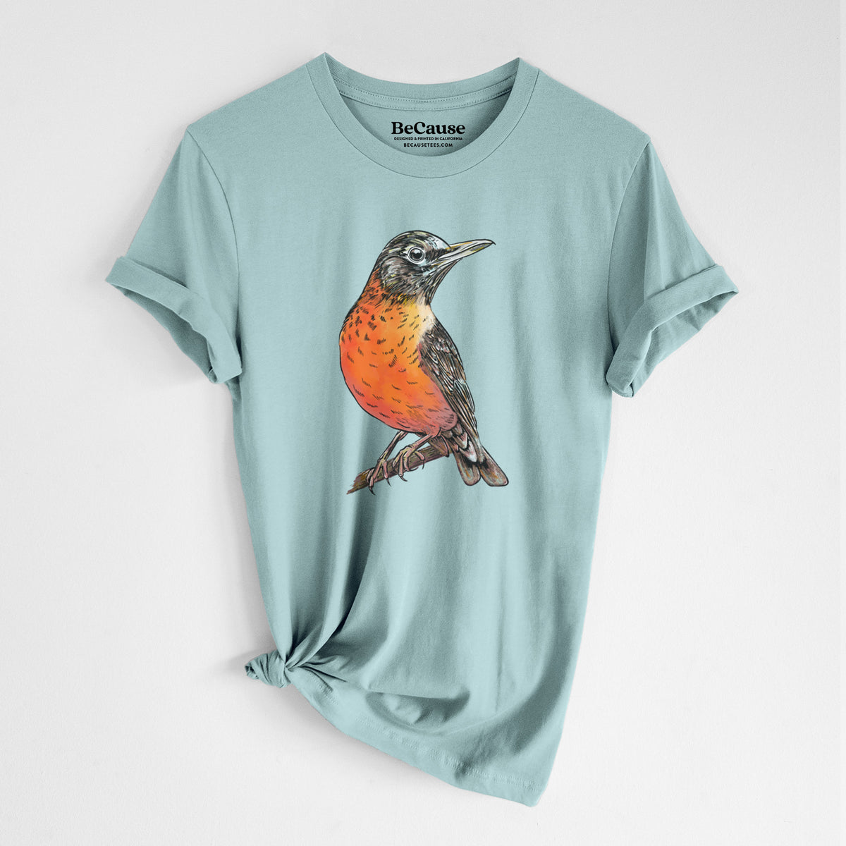 Dusty blue lightweight cotton t-shirt laid flat with the sleeves rolled, printed with a full-color illustration of an American robin with an orange breast perched on a branch.