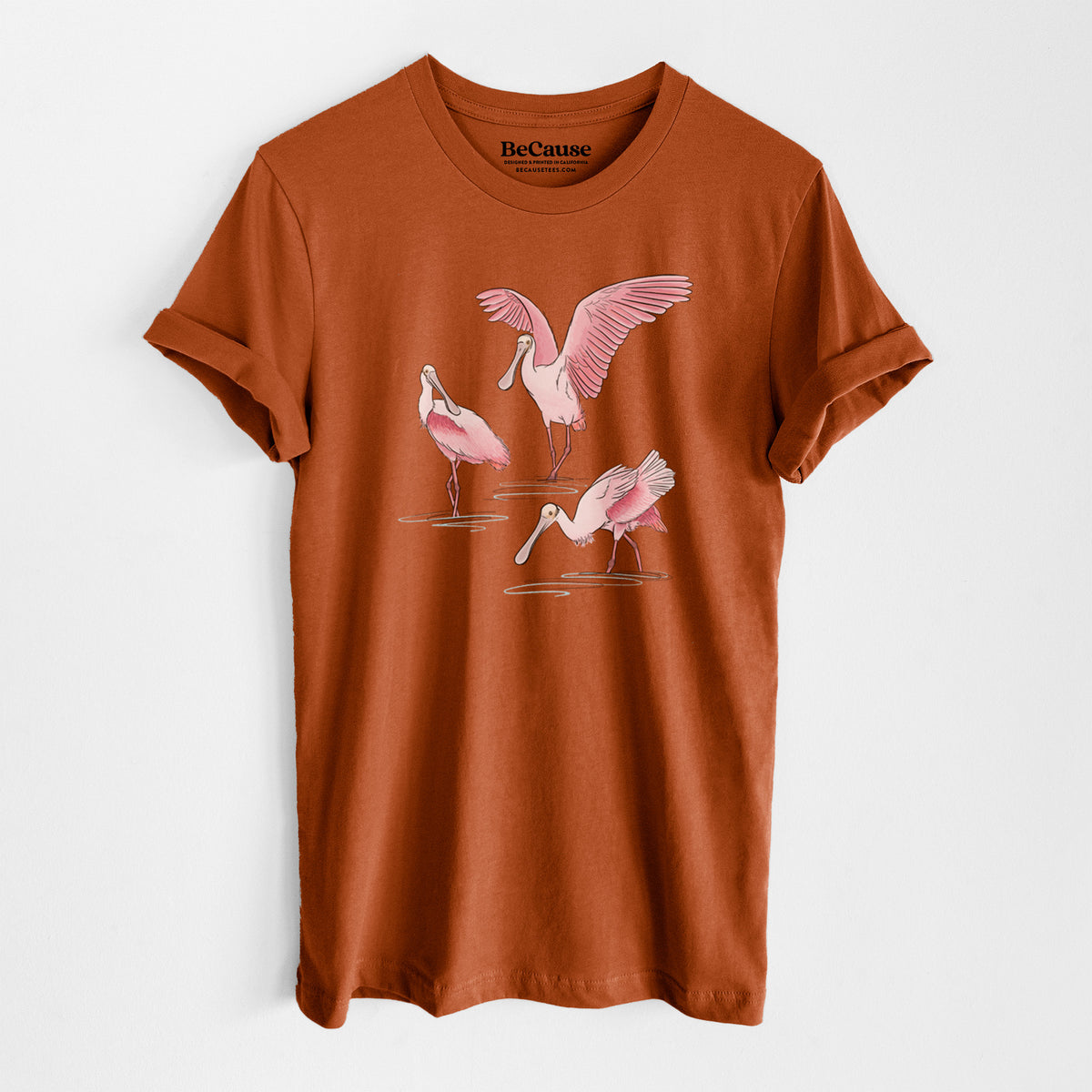 Autumn lightweight cotton t-shirt laid flat, printed with a full-color illustration of three pink roseate spoonbills wading, one with its wings spread.