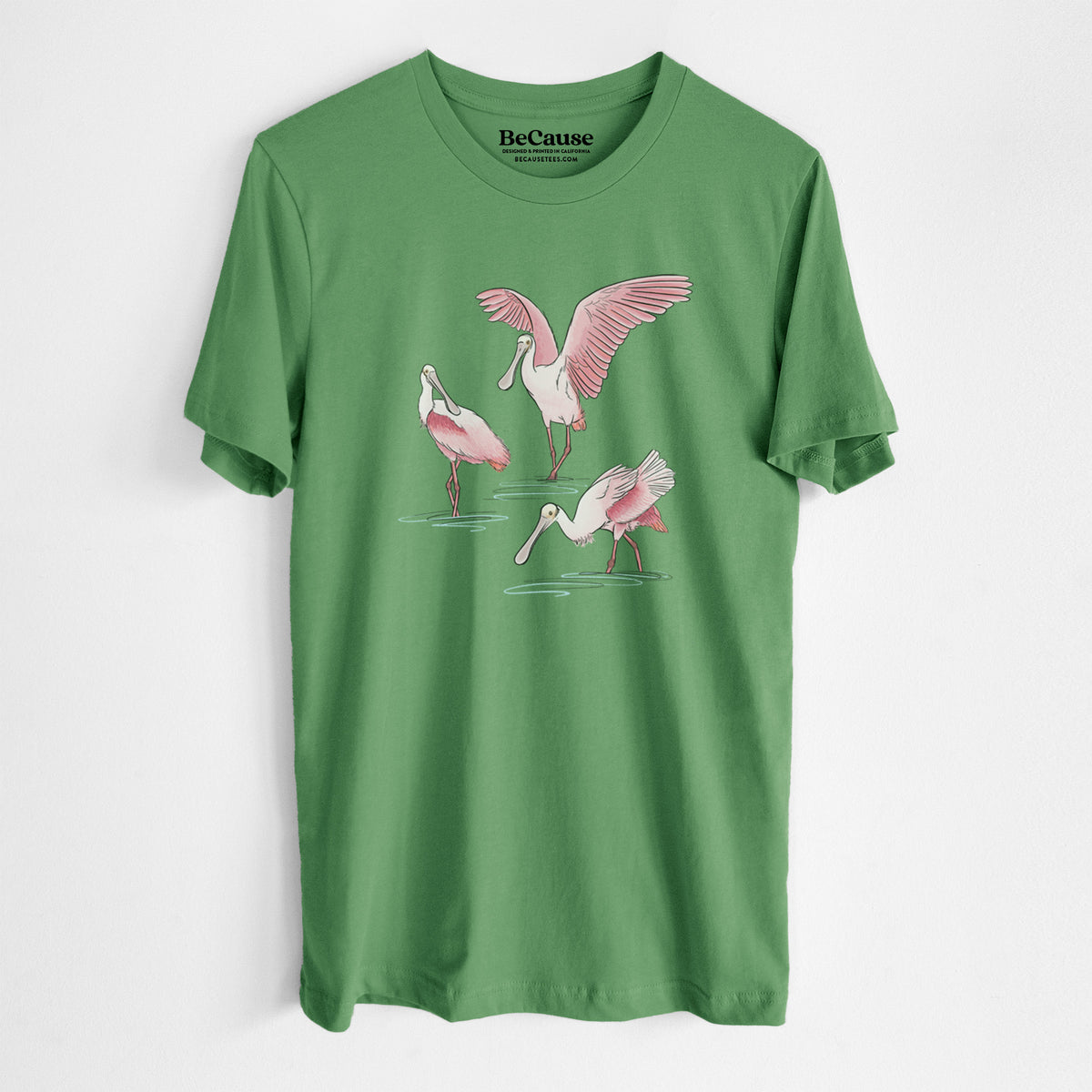Leaf green lightweight cotton t-shirt laid flat, printed with a full-color illustration of three pink roseate spoonbills wading, one with its wings spread.