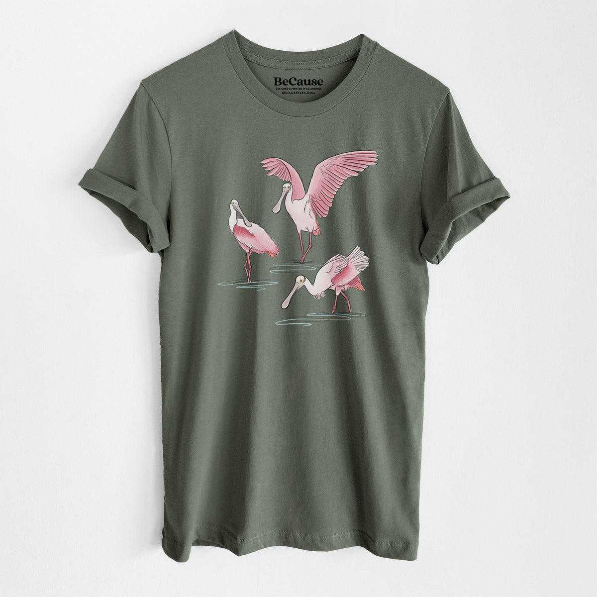 Military green lightweight cotton t-shirt laid flat, printed with a full-color illustration of three pink roseate spoonbills wading, one with its wings spread.