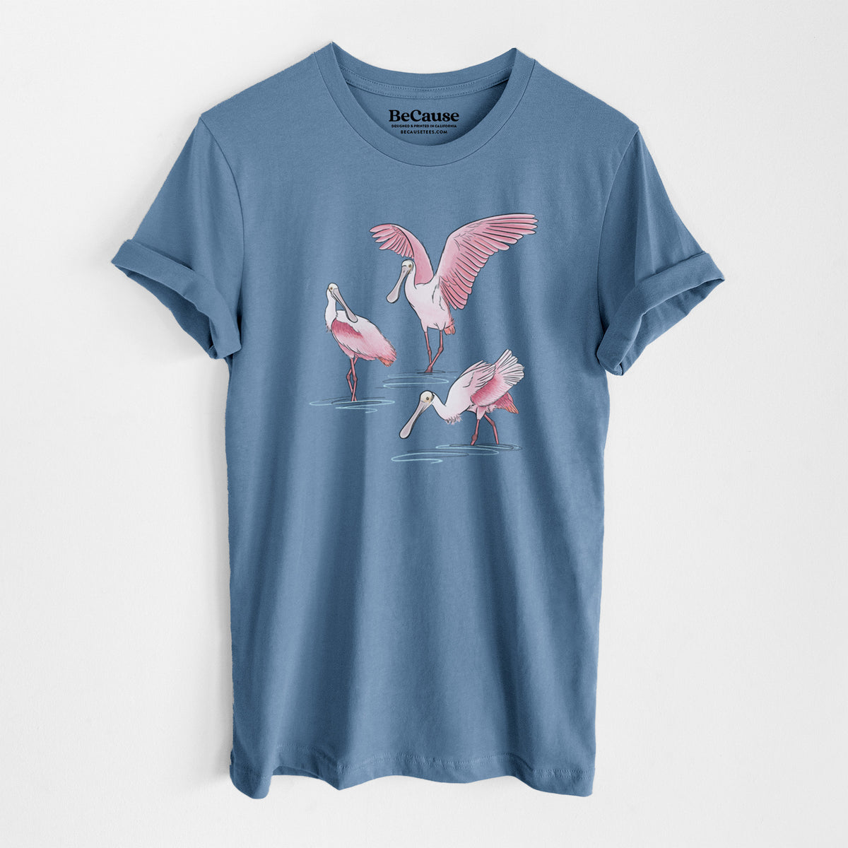 Steel blue lightweight cotton t-shirt laid flat, printed with a full-color illustration of three pink roseate spoonbills wading, one with its wings spread.