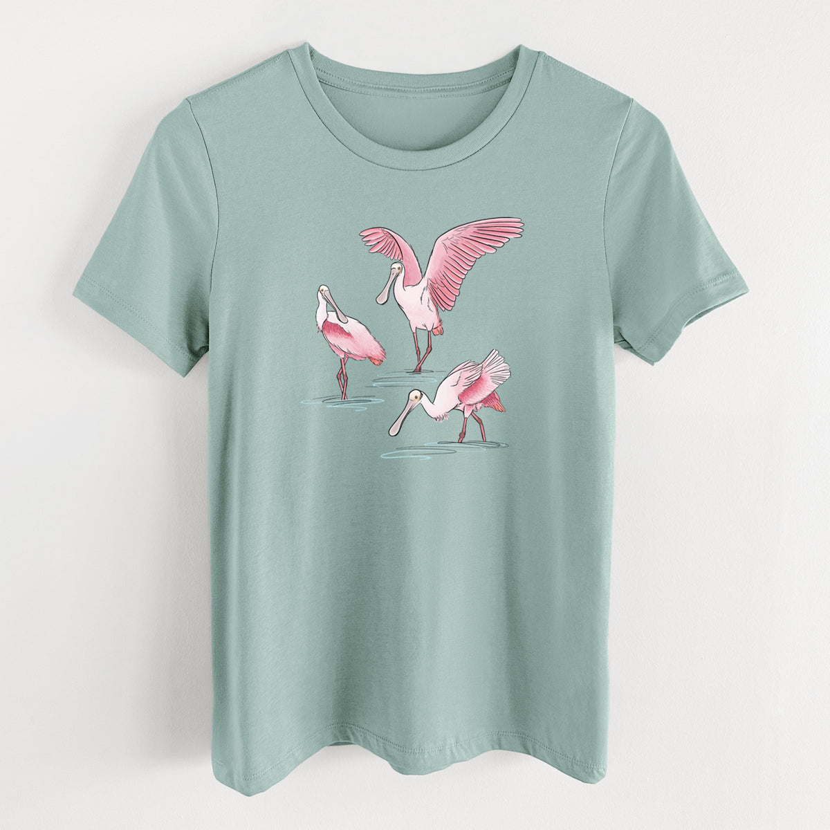 Dusty blue women's relaxed fit cotton t-shirt laid flat, printed with a full-color illustration of three pink roseate spoonbills wading, one with its wings spread.