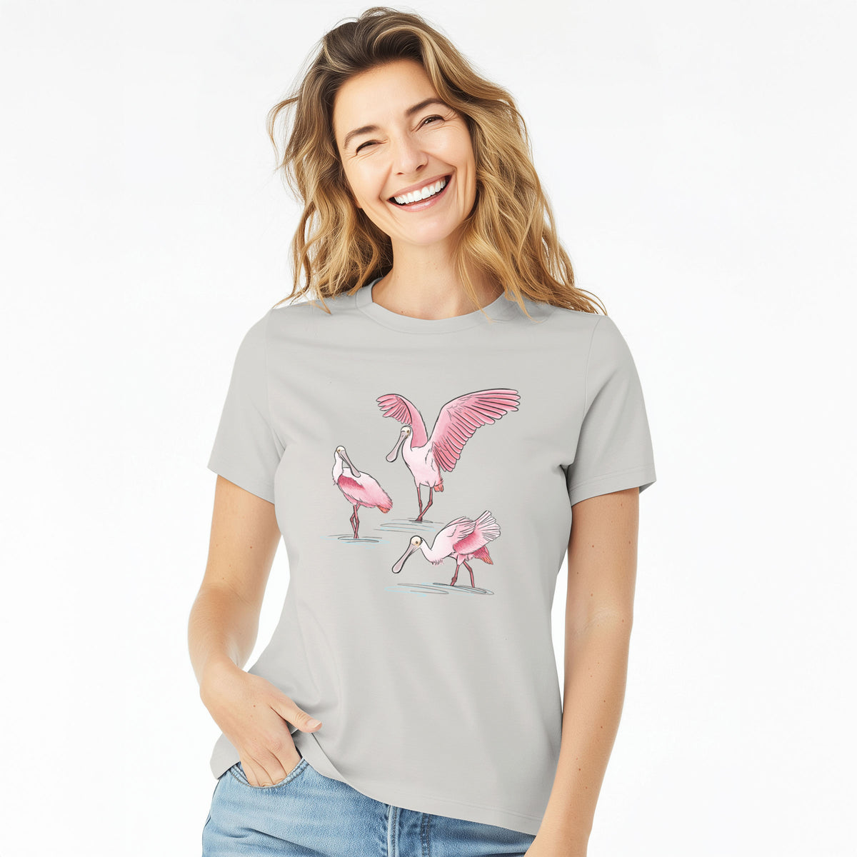 Woman wearing a lunar grey women's relaxed fit cotton t-shirt printed with a full-color illustration of three pink roseate spoonbills wading, one with its wings spread.