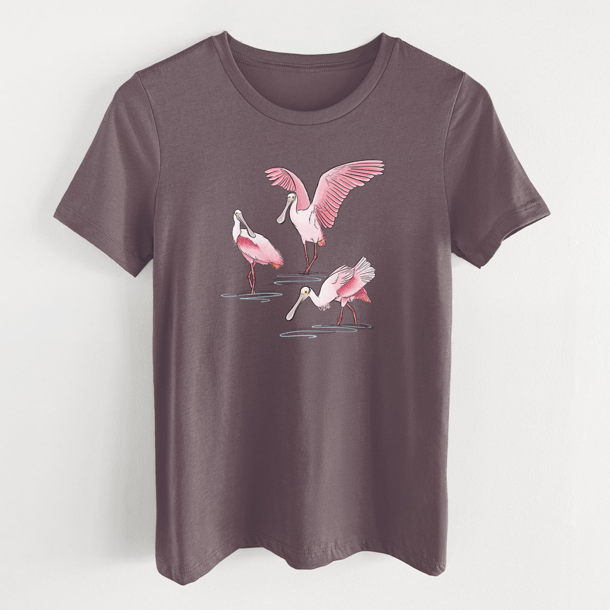Purple storm women's relaxed fit cotton t-shirt laid flat, printed with a full-color illustration of three pink roseate spoonbills wading, one with its wings spread.