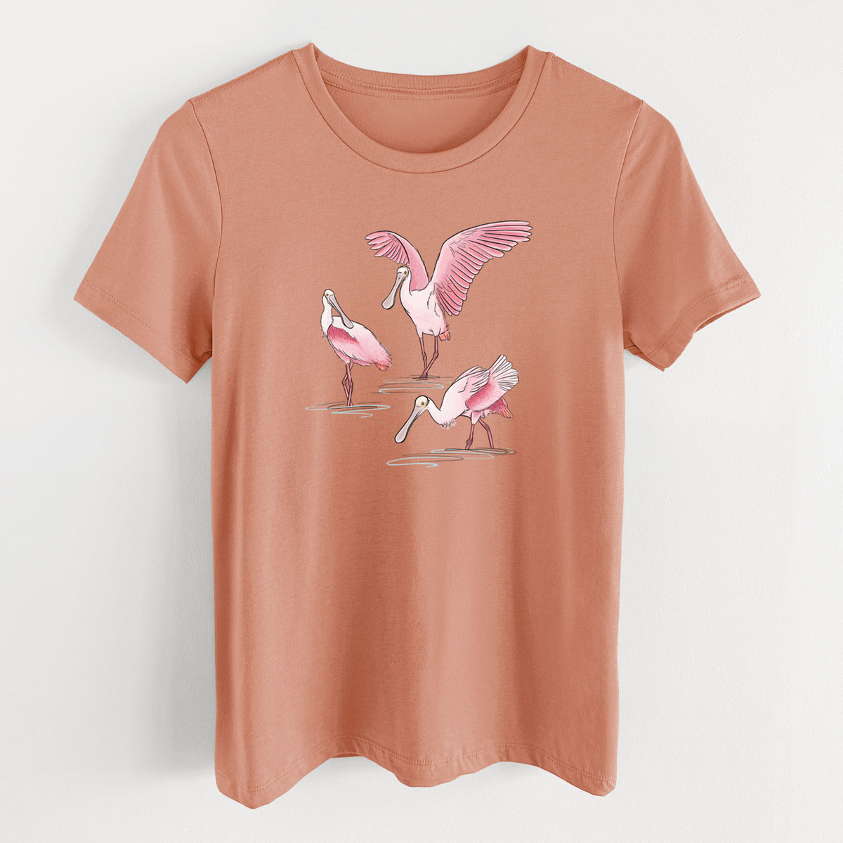Terracotta orange women's relaxed fit cotton t-shirt laid flat, printed with a full-color illustration of three pink roseate spoonbills wading, one with its wings spread.