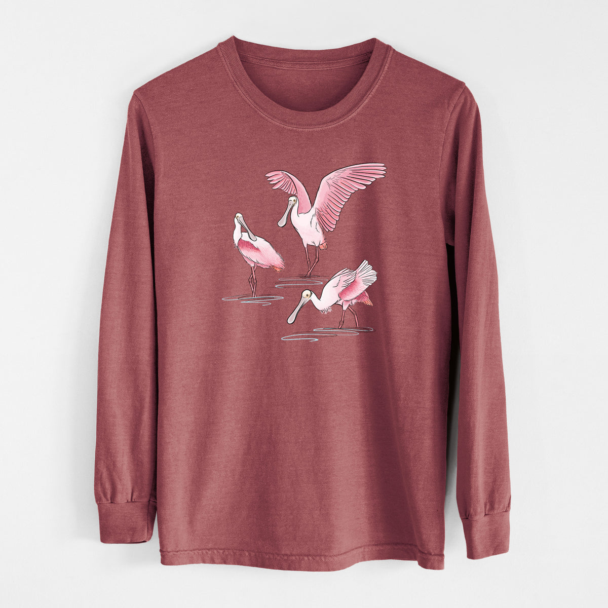 Brick red Comfort Colors long sleeve shirt laid flat, printed with a full-color illustration of three pink roseate spoonbills wading, one with its wings spread.