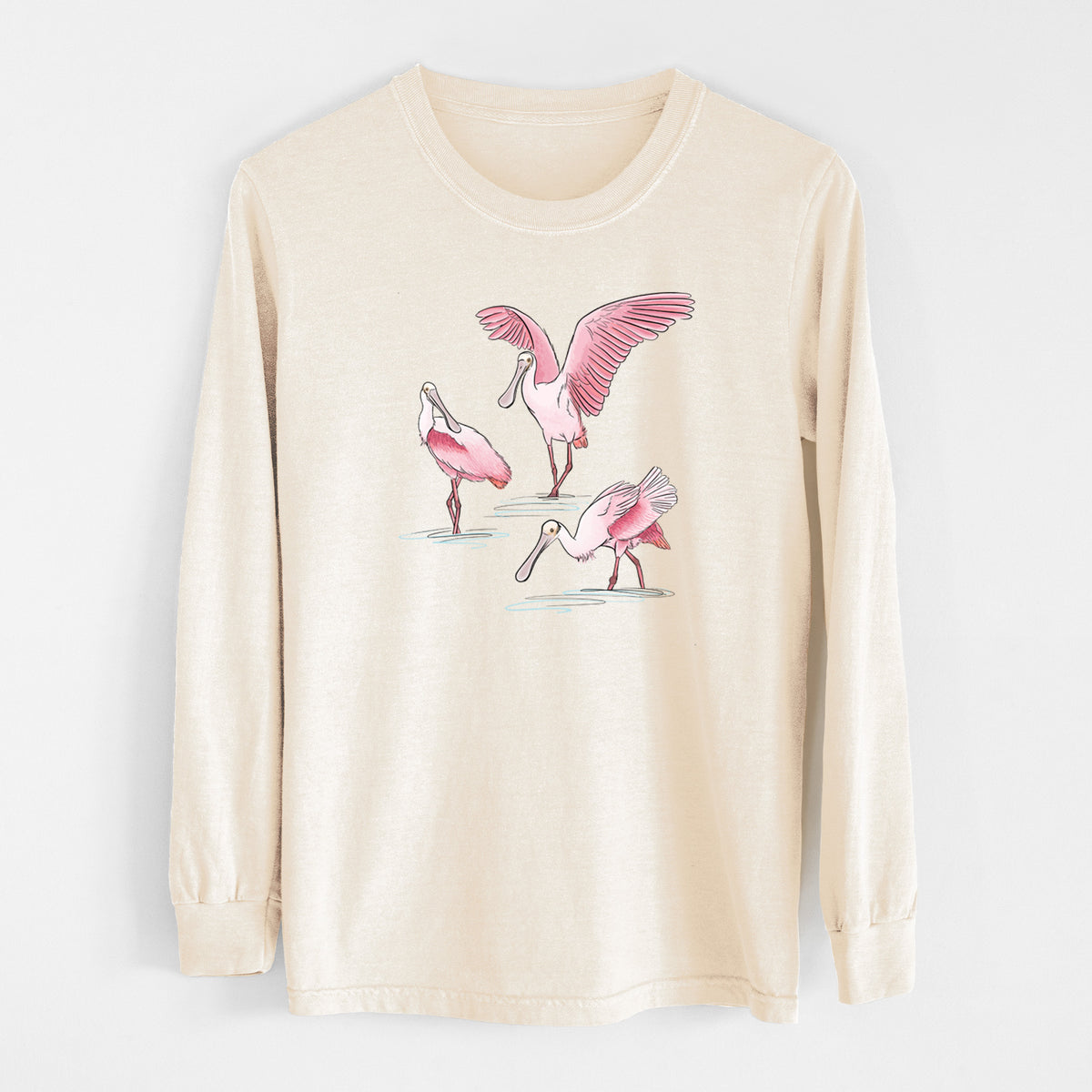Ivory Comfort Colors long sleeve shirt laid flat, printed with a full-color illustration of three pink roseate spoonbills wading, one with its wings spread.