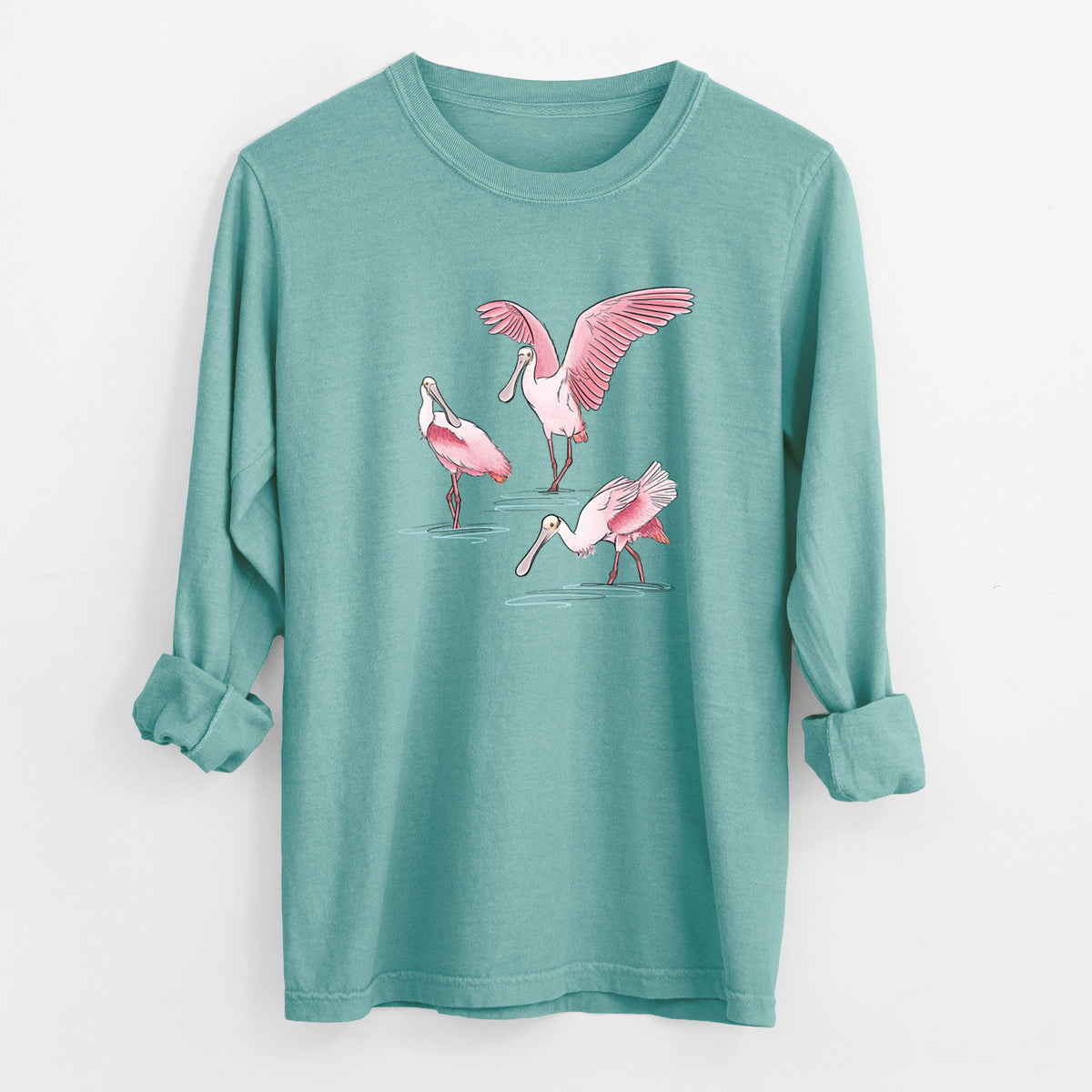 Reef green Comfort Colors long sleeve shirt laid flat with the cuffs rolled, printed with a full-color illustration of three pink roseate spoonbills wading, one with its wings spread.