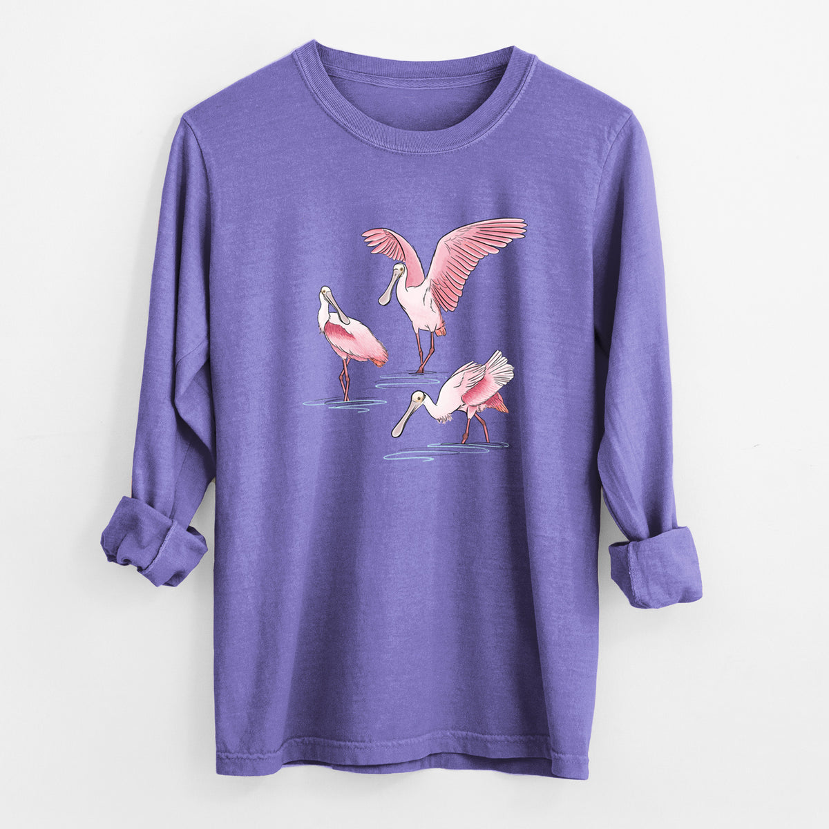 Violet purple Comfort Colors long sleeve shirt laid flat with the cuffs rolled, printed with a full-color illustration of three pink roseate spoonbills wading, one with its wings spread.