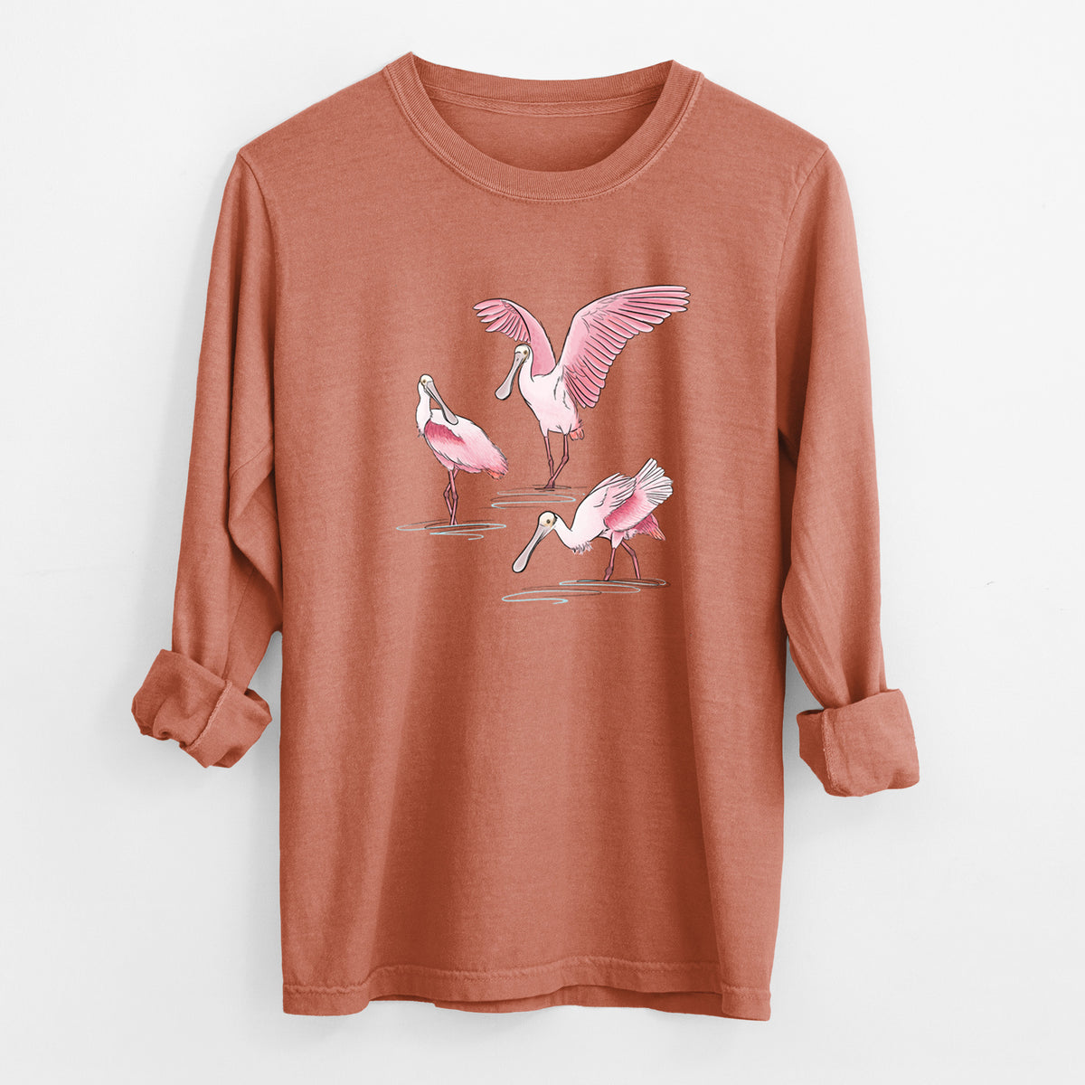 Yam burnt orange Comfort Colors long sleeve shirt laid flat with the cuffs rolled, printed with a full-color illustration of three pink roseate spoonbills wading, one with its wings spread.