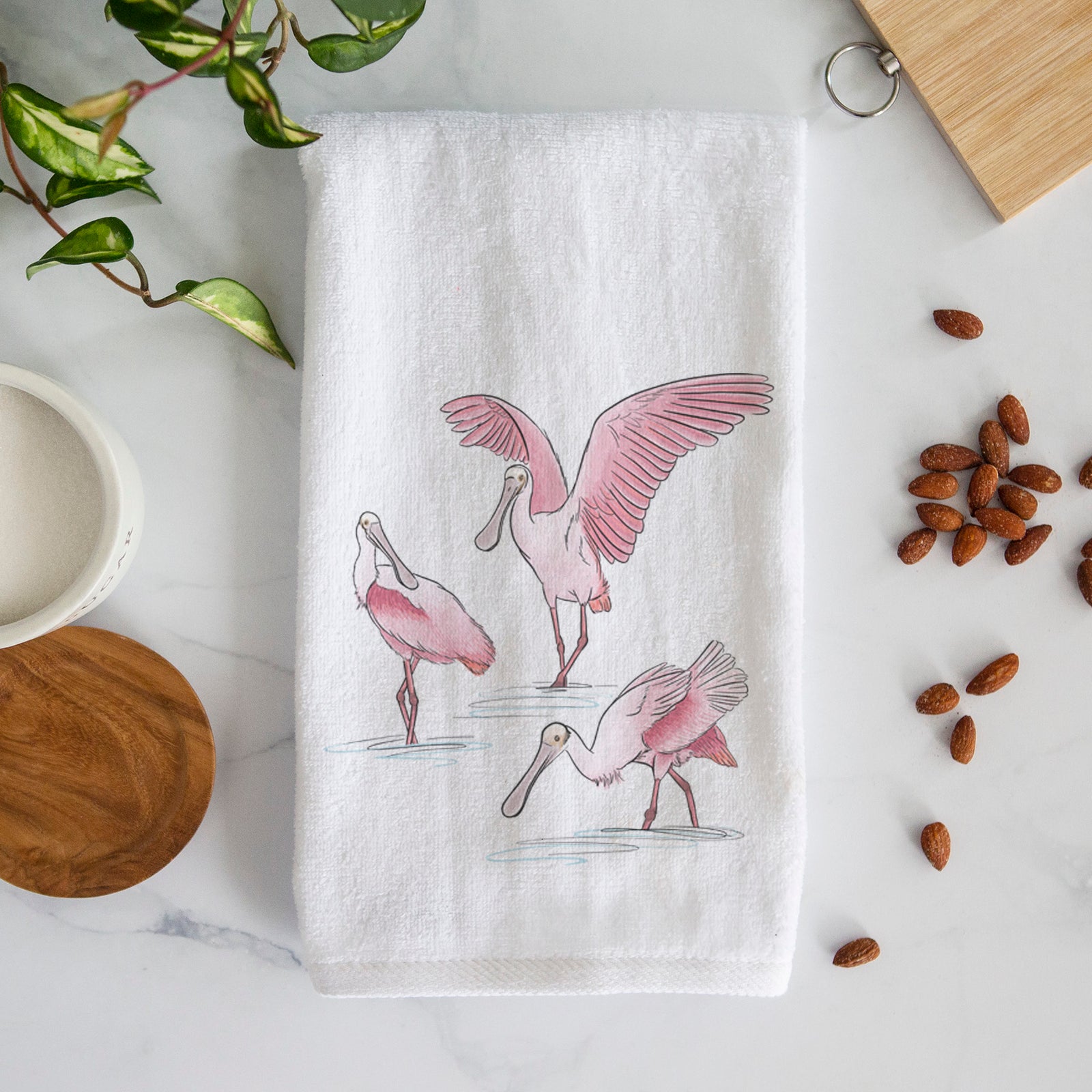 White hand towel printed with a full-color illustration of three pink roseate spoonbills wading, one with its wings spread.