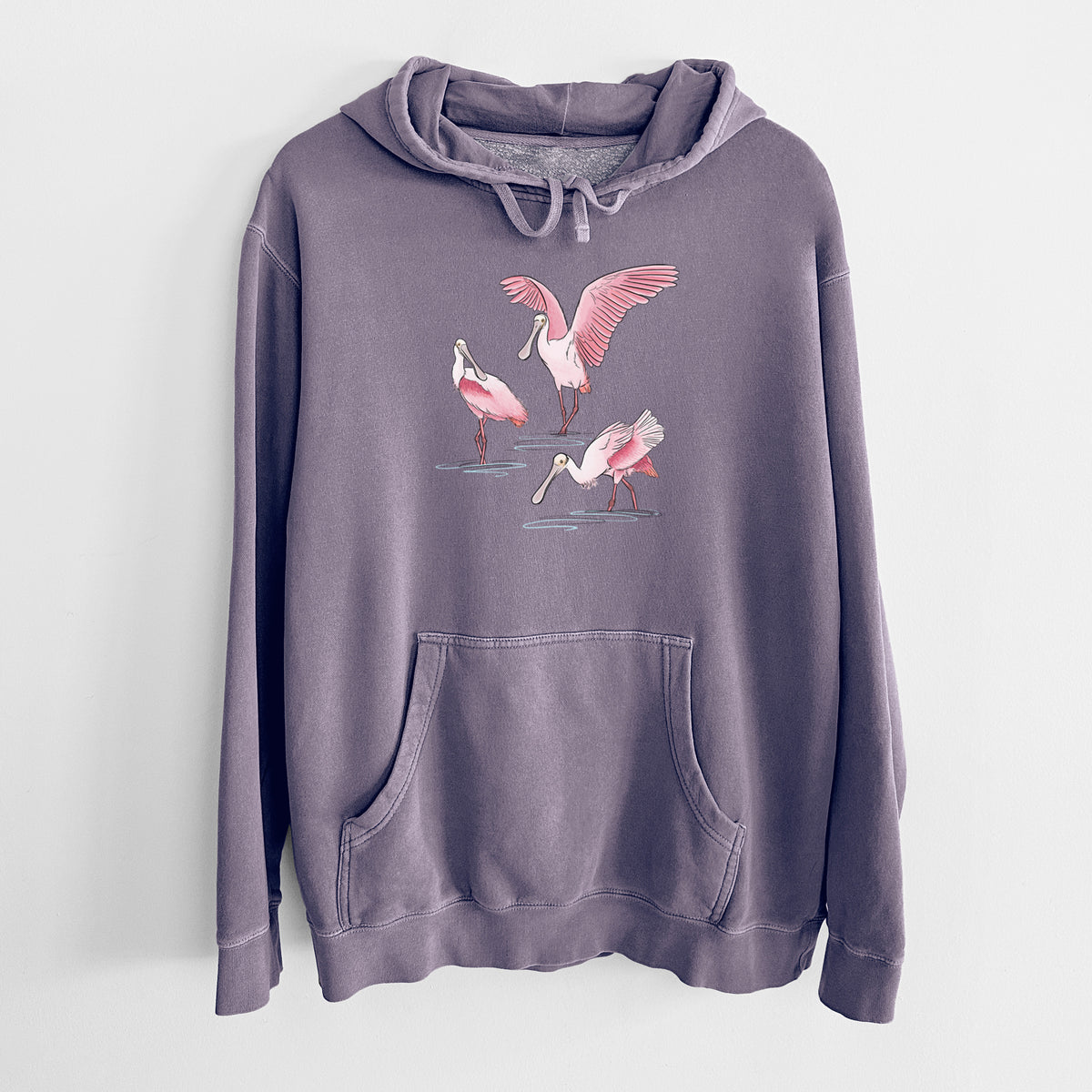 Plum purple pigment dyed hoodie laid flat, printed with a full-color illustration of three pink roseate spoonbills wading, one with its wings spread.