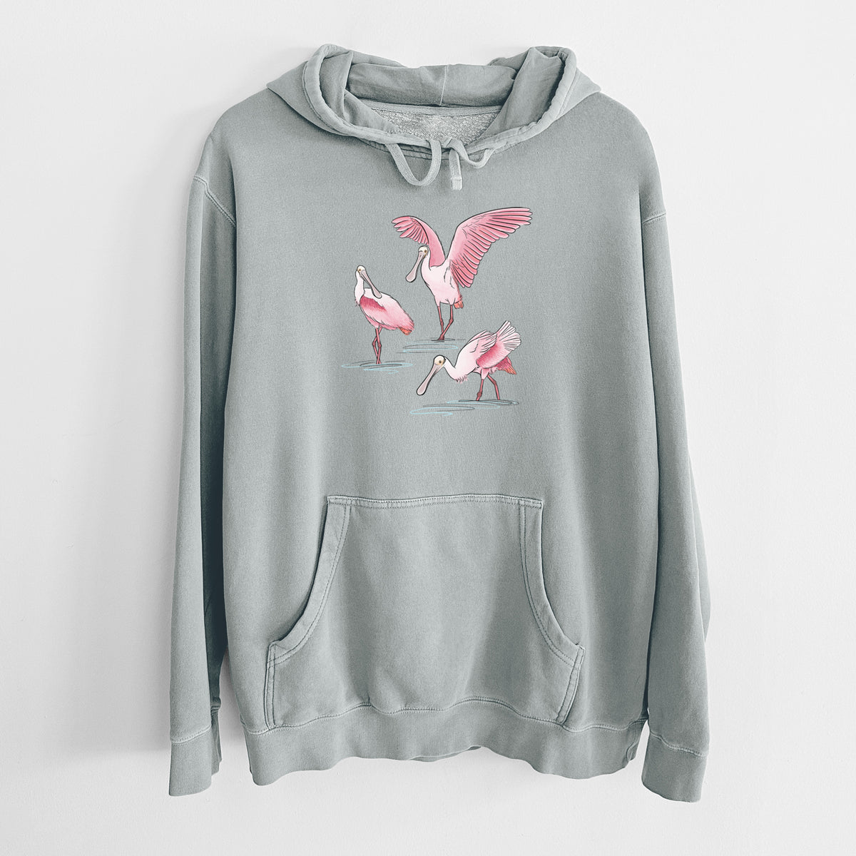 Sage green pigment dyed hoodie laid flat, printed with a full-color illustration of three pink roseate spoonbills wading, one with its wings spread.