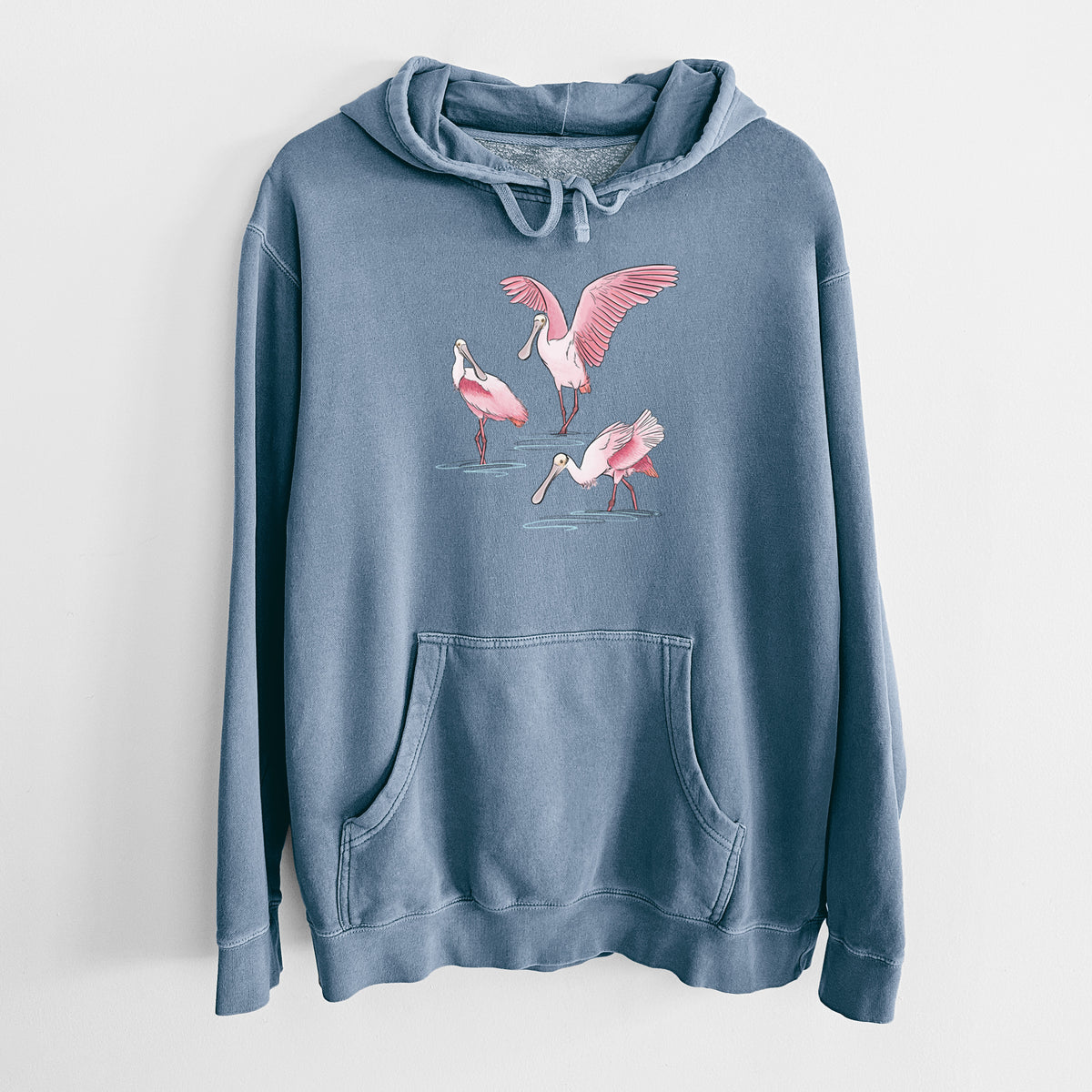 Slate blue pigment dyed hoodie laid flat, printed with a full-color illustration of three pink roseate spoonbills wading, one with its wings spread.