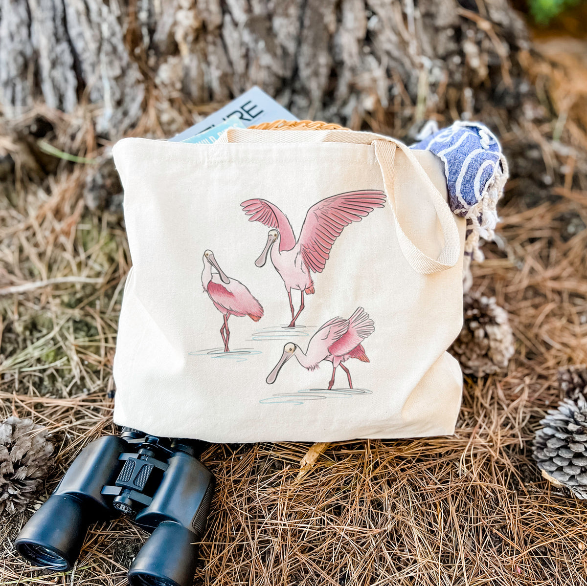 Canvas tote bag printed with a full-color illustration of three pink roseate spoonbills wading, one with its wings spread, resting on dry grass beside a pair of binoculars.