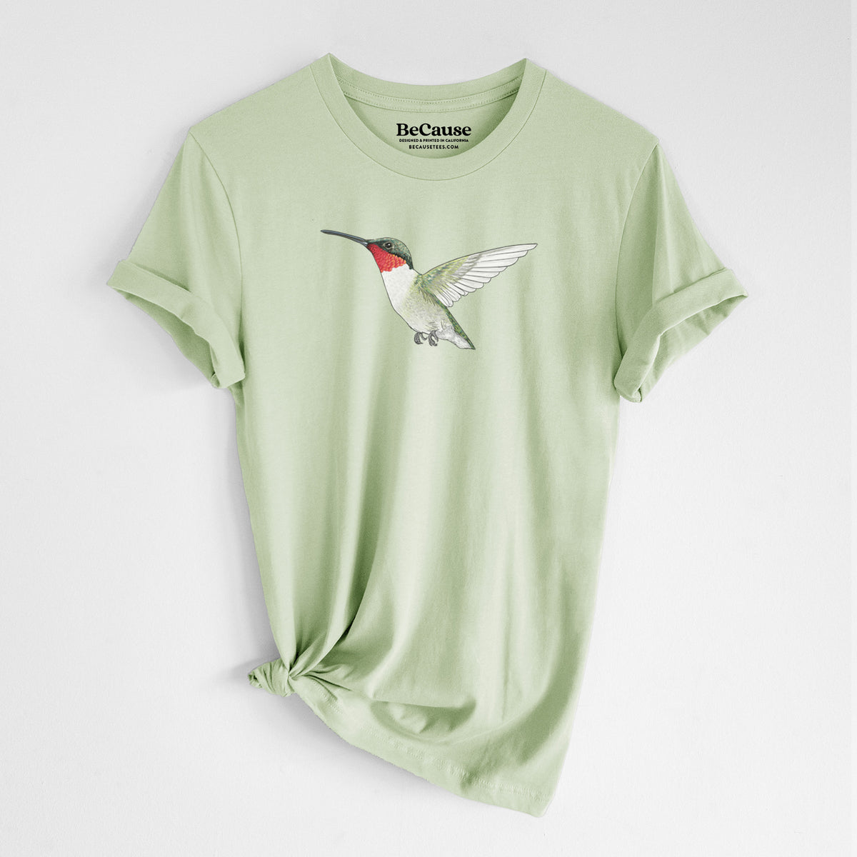 Spring green lightweight cotton t-shirt laid flat with the sleeves rolled, printed with a full-color illustration of a ruby-throated hummingbird in flight.