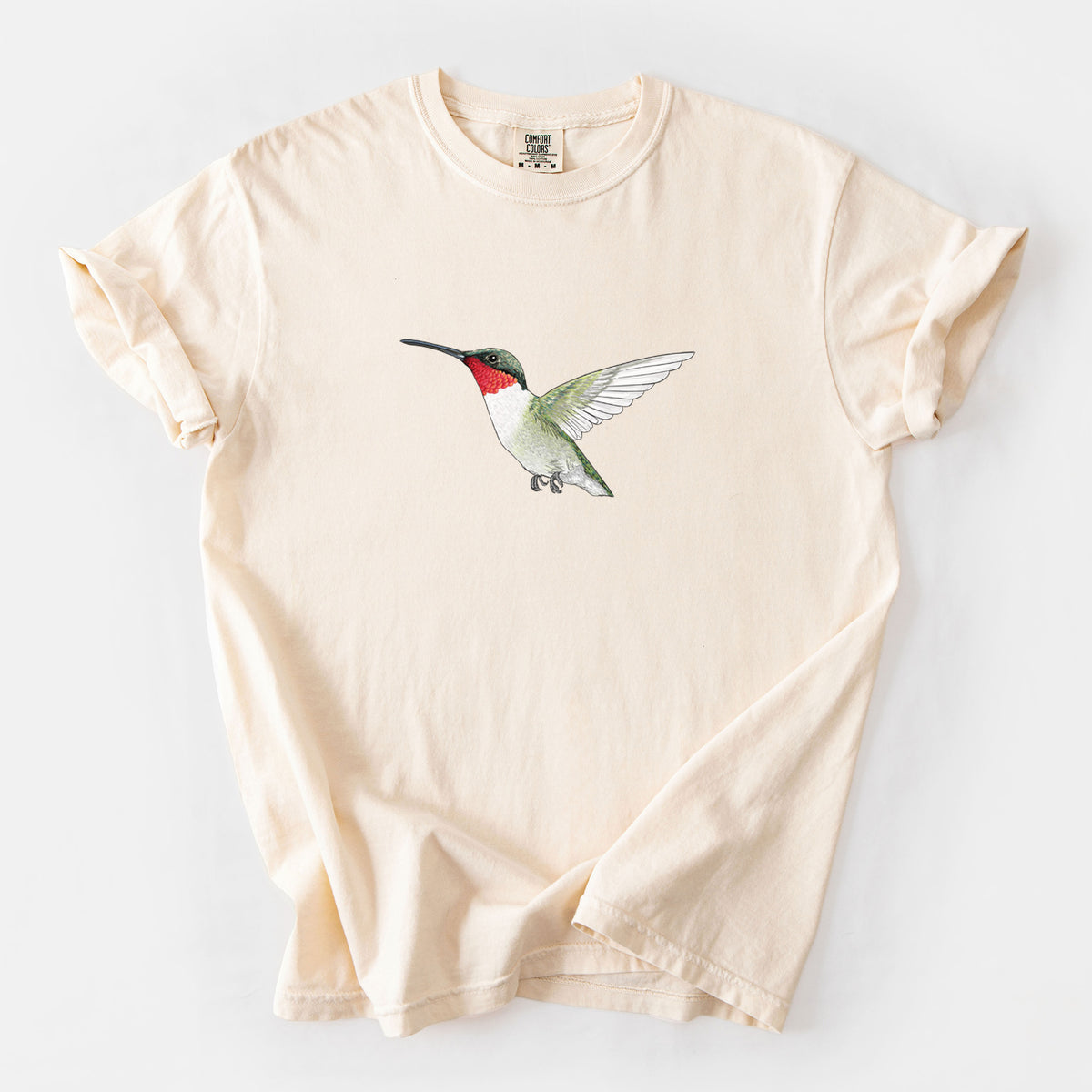Ivory Comfort Colors t-shirt laid flat, printed with a full-color illustration of a ruby-throated hummingbird in flight.