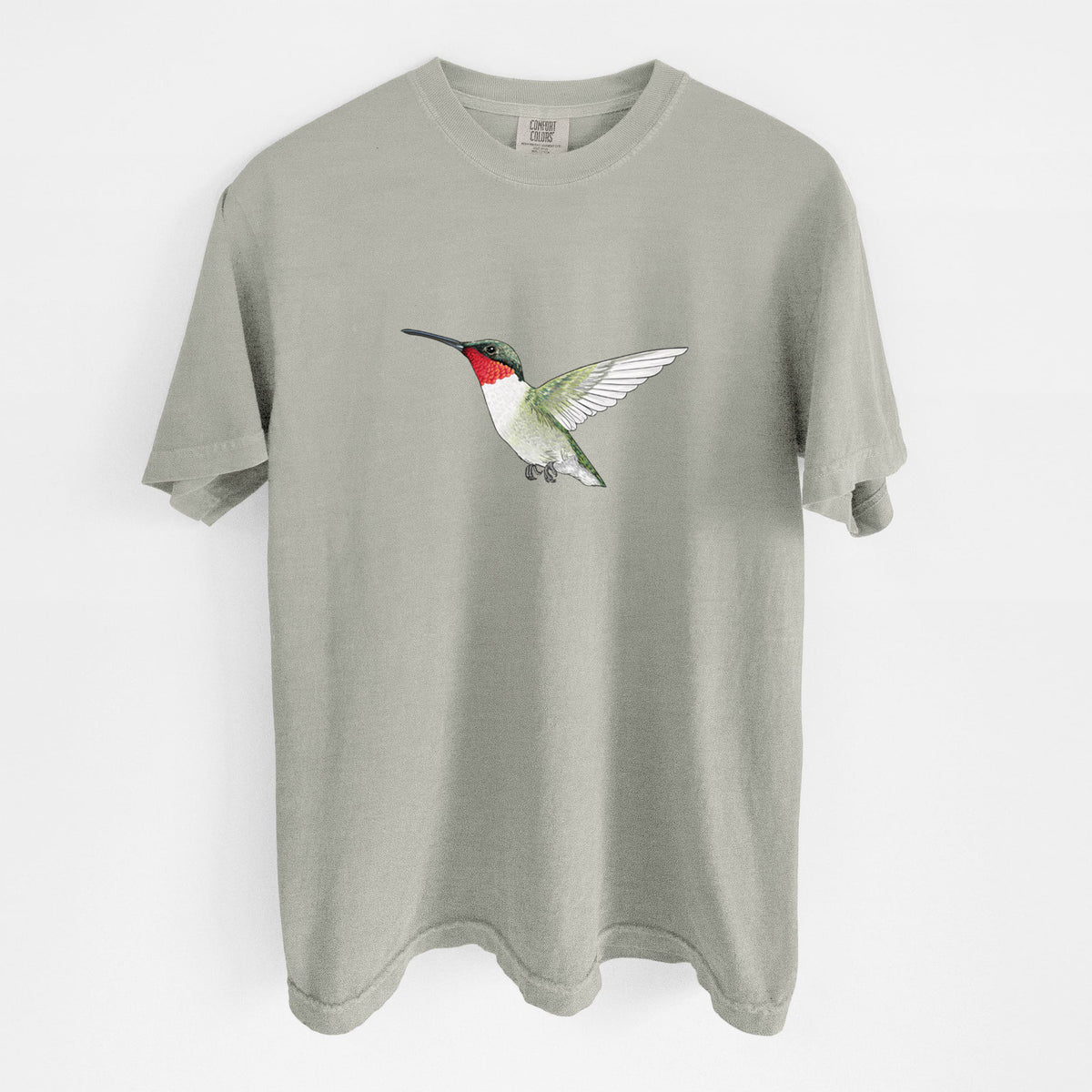Sandstone beige Comfort Colors t-shirt laid flat, printed with a full-color illustration of a ruby-throated hummingbird in flight.