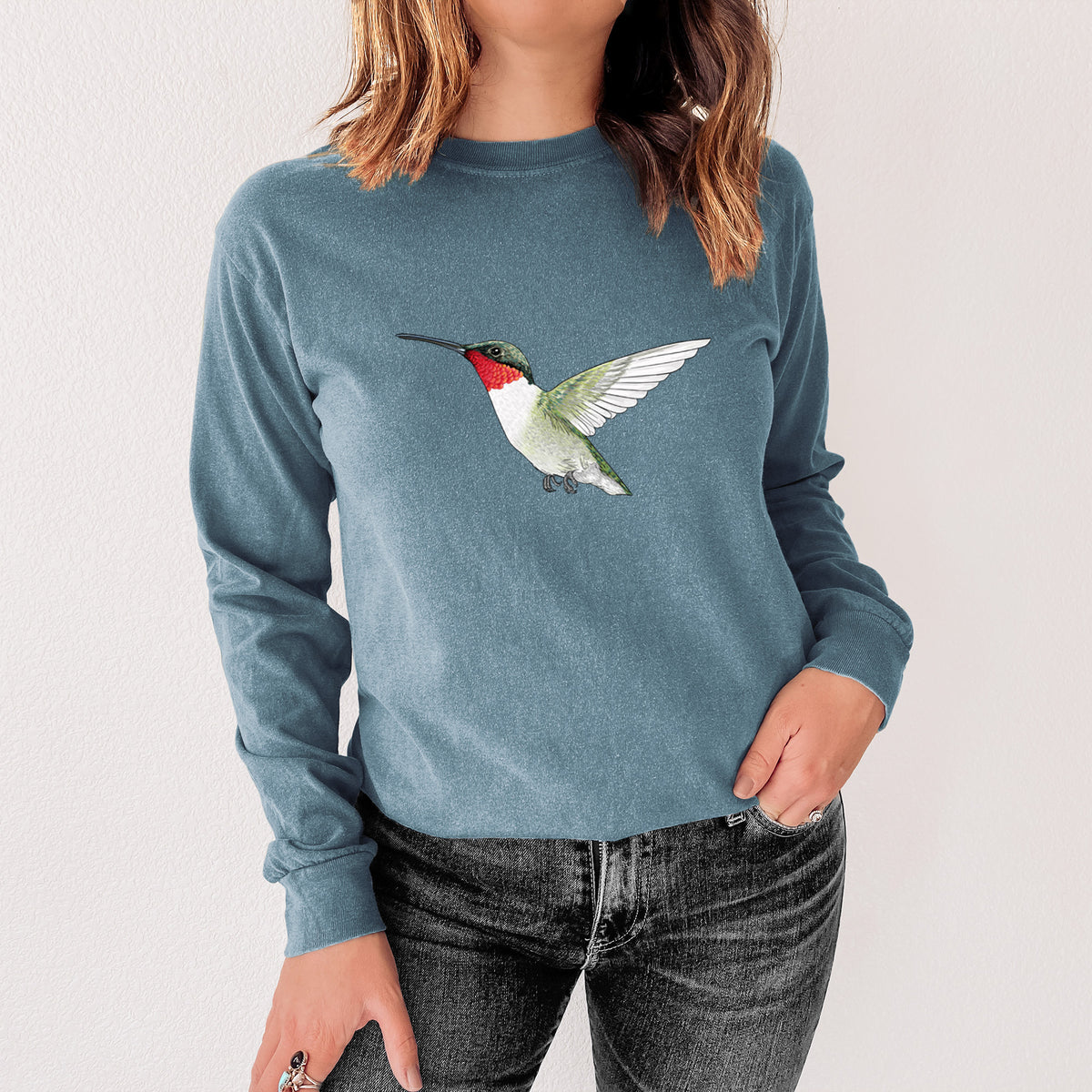 Steel blue Comfort Colors long sleeve shirt printed with a full-color illustration of a ruby-throated hummingbird in flight, shown in a lifestyle photo.