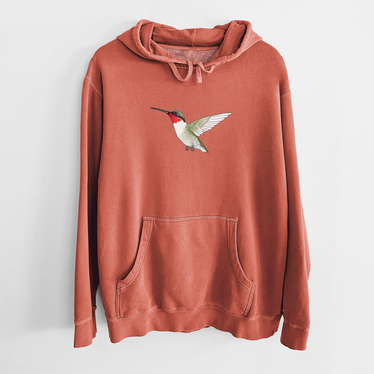 Amber orange pigment dyed hoodie laid flat, printed with a full-color illustration of a ruby-throated hummingbird in flight.