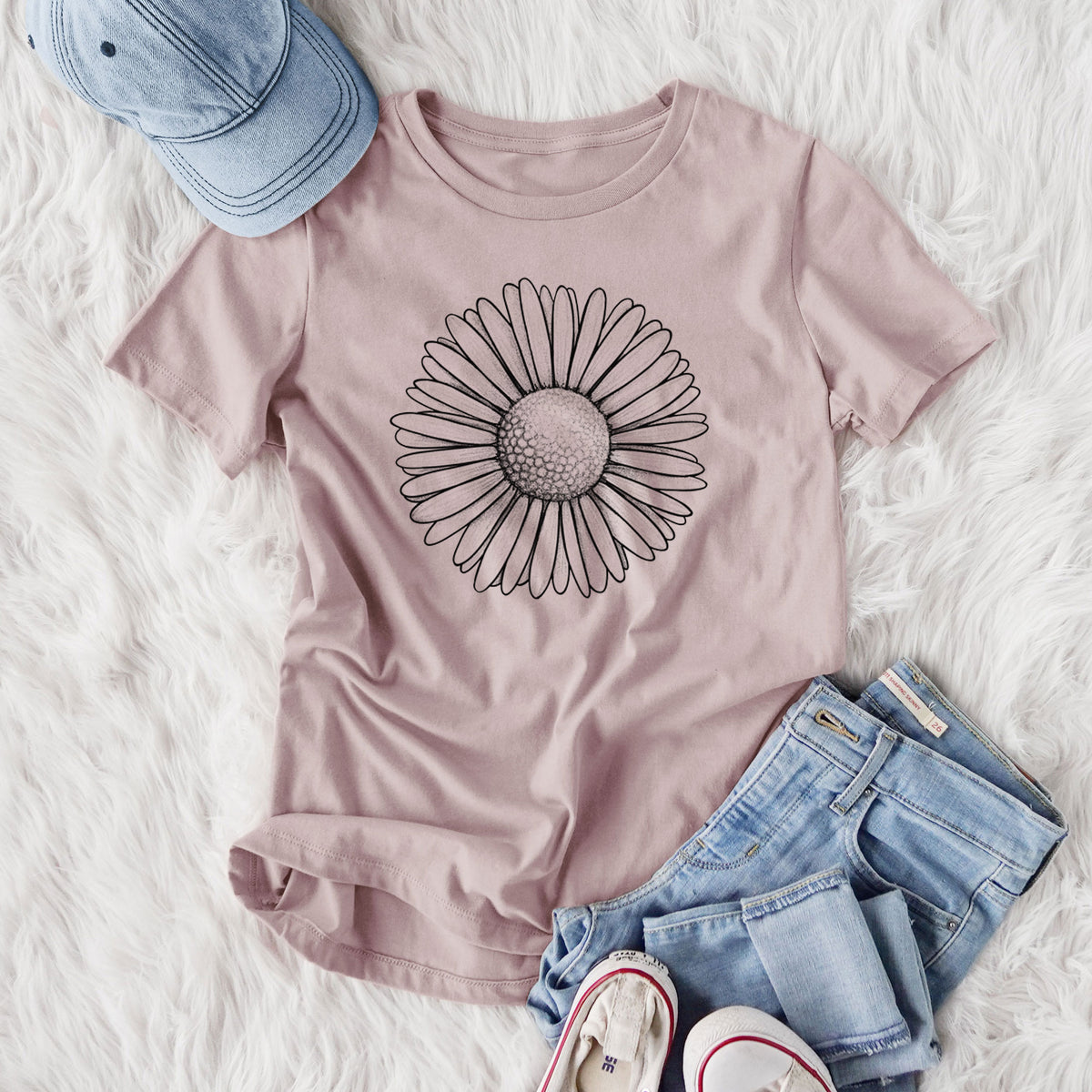 Women's relaxed fit cotton t-shirt printed with a detailed black ink line drawing of a single common daisy flower, styled flat on a white faux fur rug with jeans.