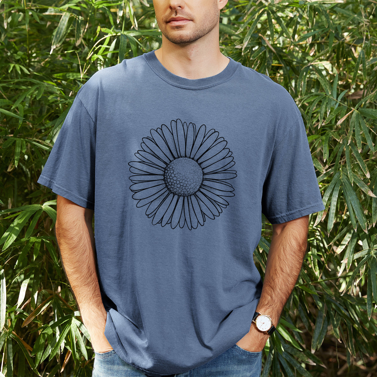 Man wearing a Comfort Colors t-shirt printed with a detailed black ink line drawing of a single common daisy flower, outdoors.