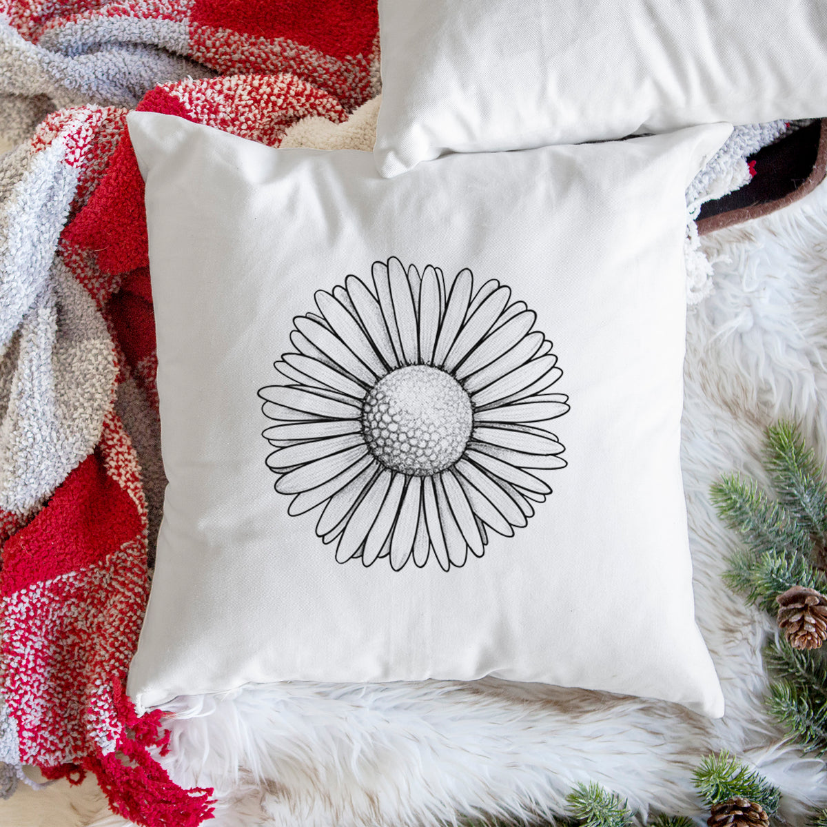 White pillow cover printed with a detailed black ink line drawing of a single common daisy flower, on a woven chair.