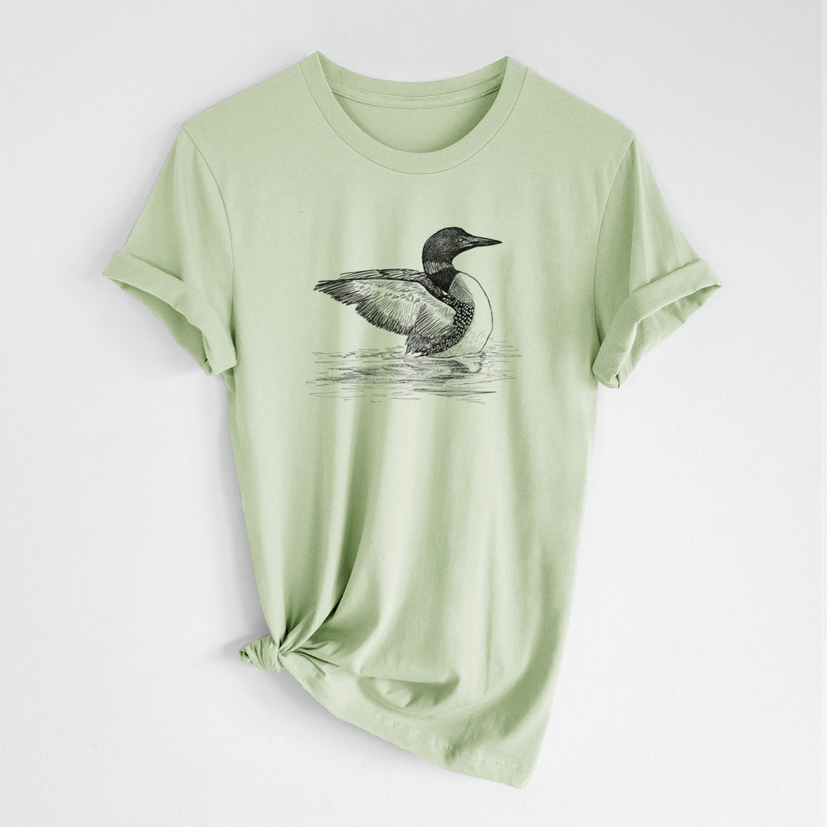Spring green lightweight cotton t-shirt laid flat with the sleeves rolled, printed with a detailed black ink sketch of a common loon floating on rippling water.