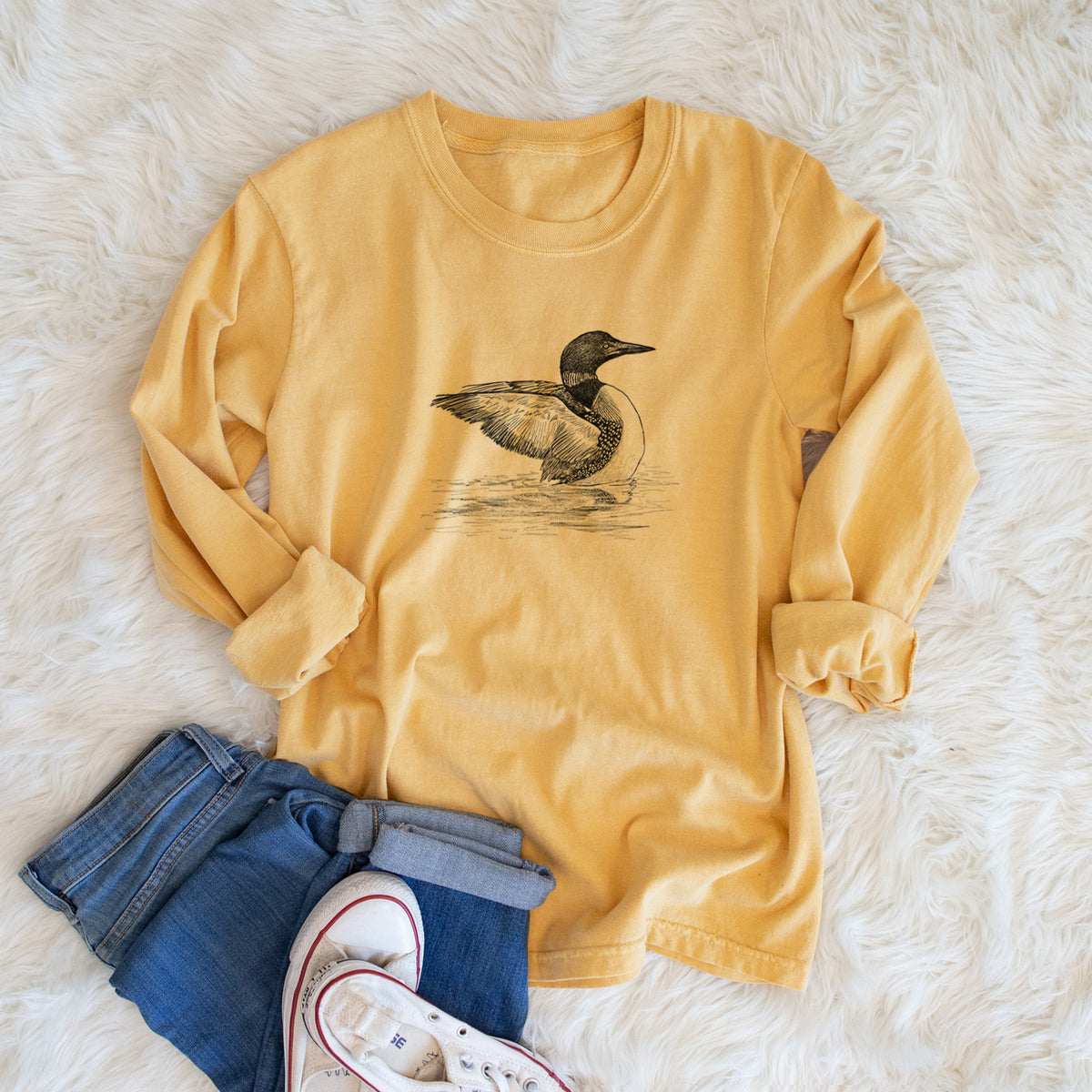 Golden wheat yellow Comfort Colors long sleeve shirt printed with a detailed black ink sketch of a common loon floating on rippling water, shown in a lifestyle photo.
