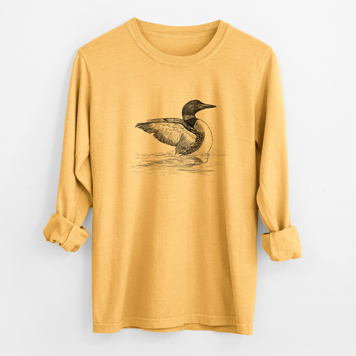 Golden wheat yellow Comfort Colors long sleeve shirt laid flat with the cuffs rolled, printed with a detailed black ink sketch of a common loon floating on rippling water.